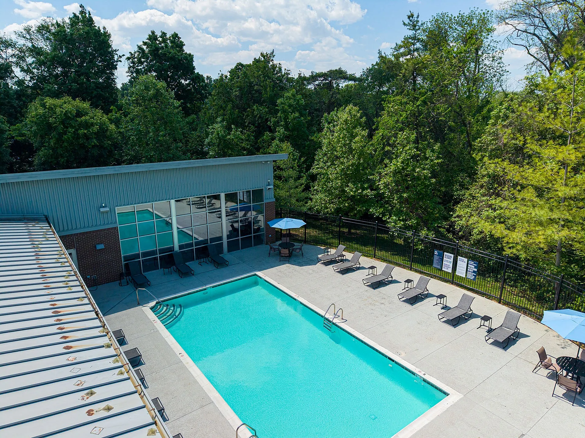 Inviting outdoor pool area with lounge chairs and a modern building backdrop, surrounded by lush greenery.