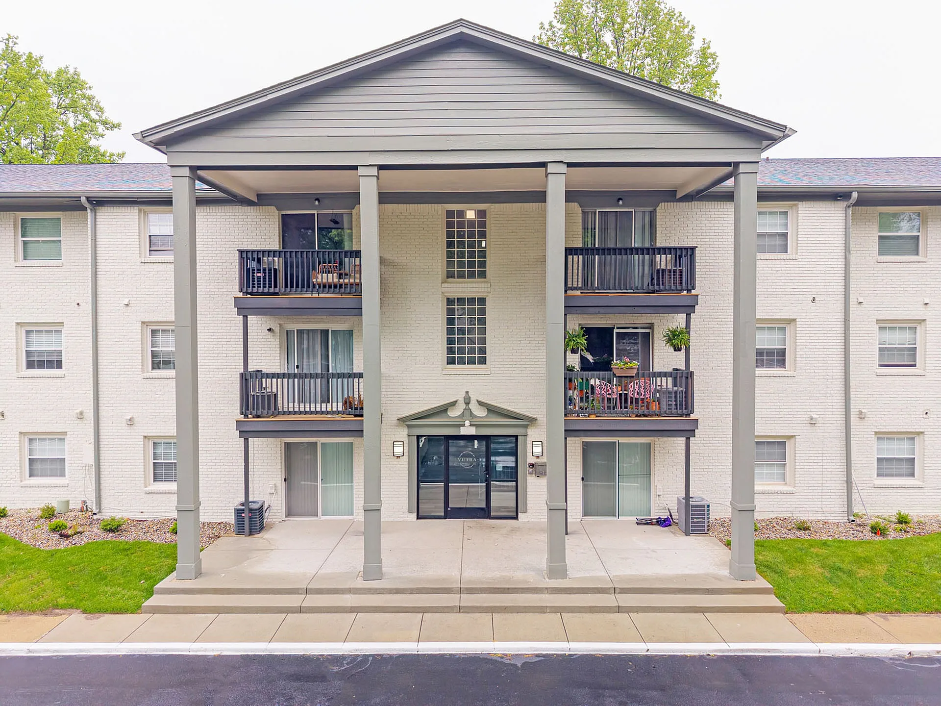 Charming apartment building with elegant balconies, lush greenery, and stylish brick facade, promising a warm and inviting community atmosphere.