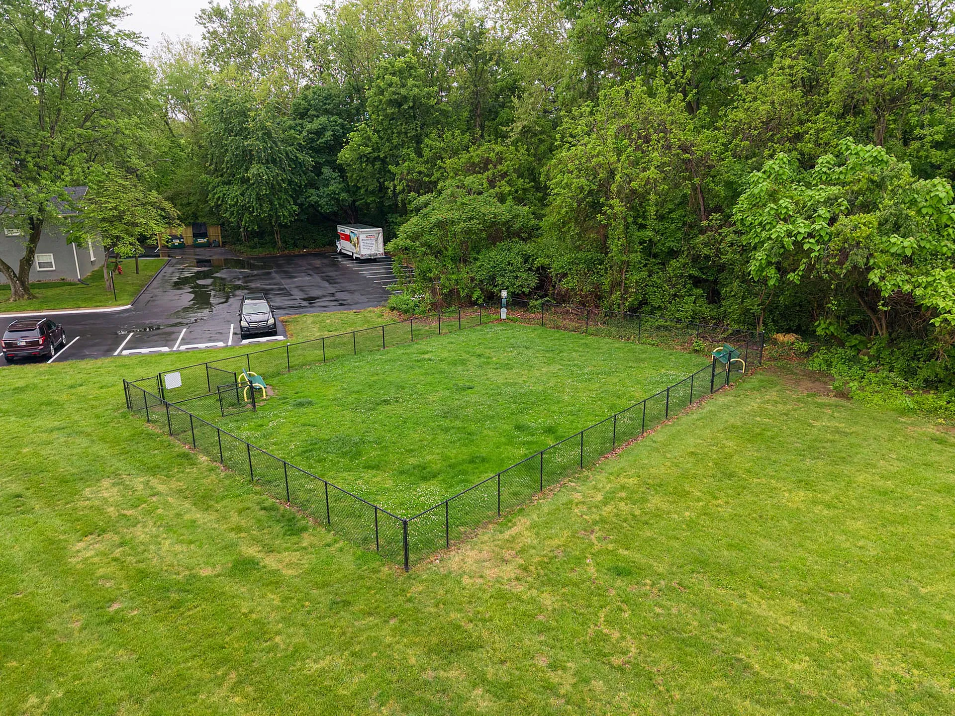 Charming fenced green space with lush trees, perfect for outdoor relaxation, next to a convenient parking area.