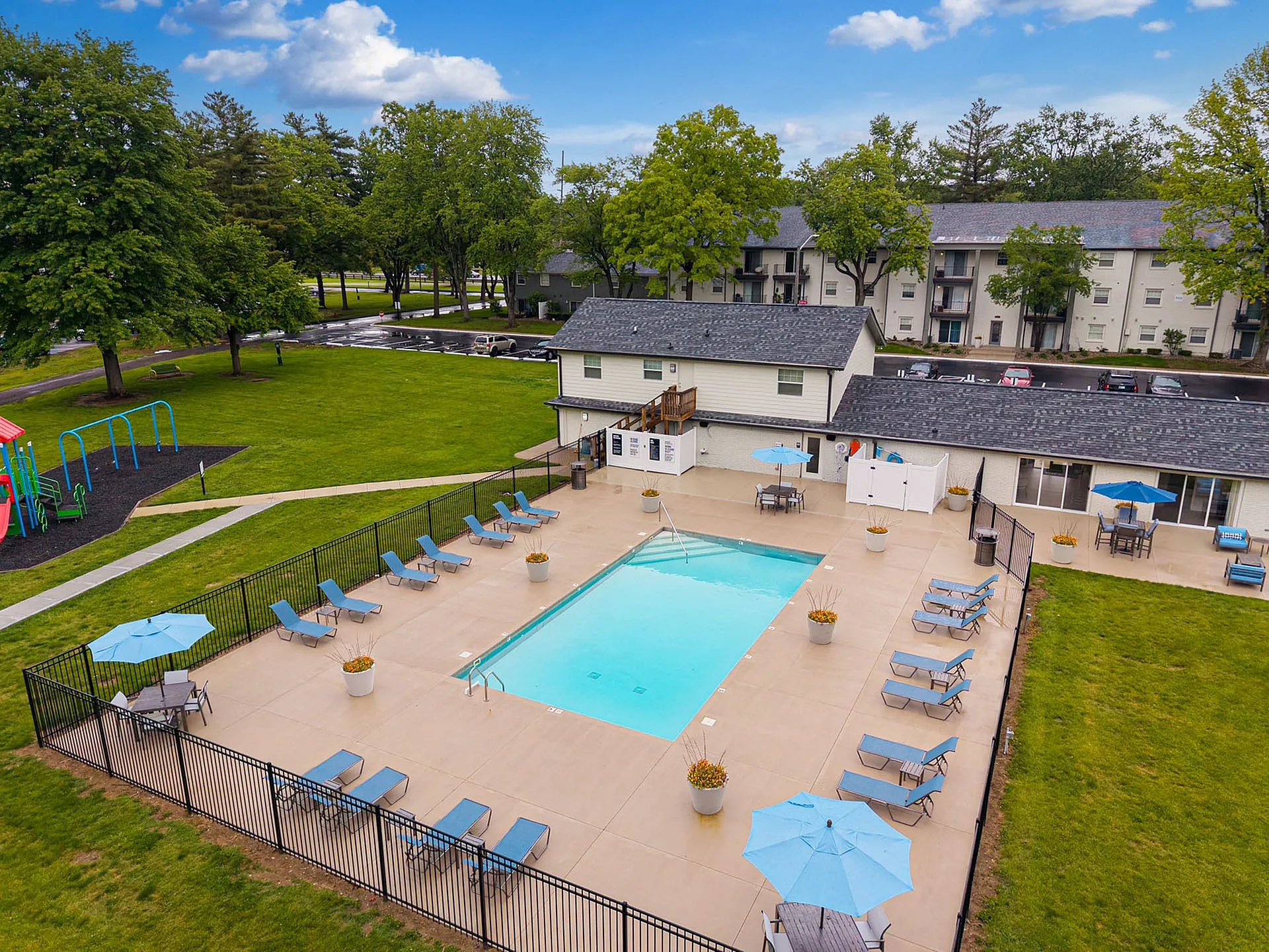 Charming apartment complex with inviting swimming pool, sun loungers, and lush play area, perfect for relaxation and family fun.