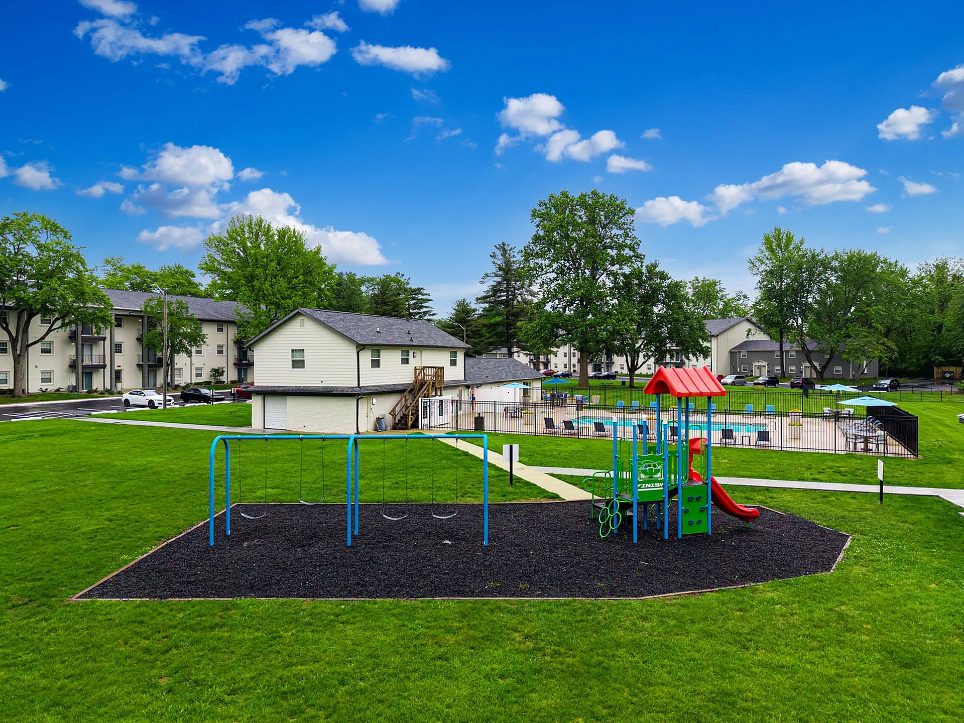 Charming apartment community with family-friendly playground and inviting swimming pool, lush green surroundings.