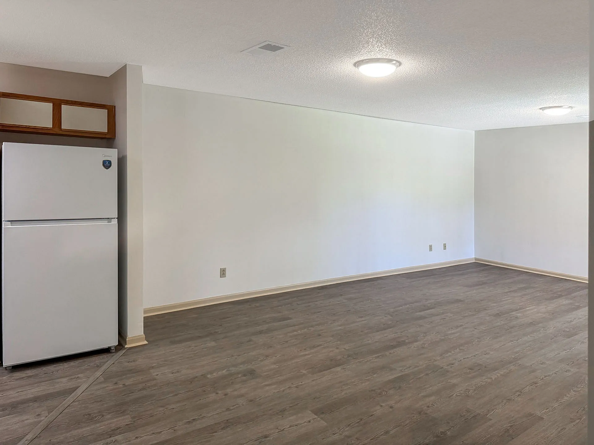 Modern open-concept apartment space with sleek flooring and ample natural light, featuring a built-in kitchen area.