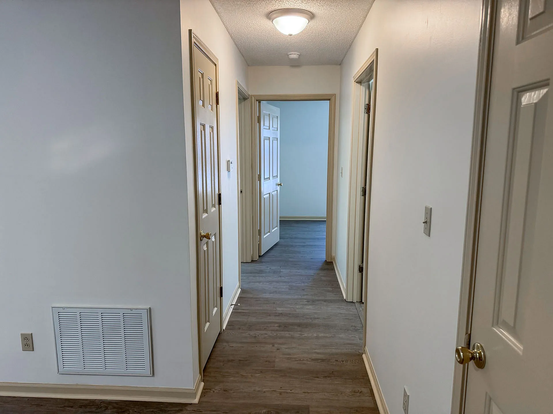 Inviting apartment hallway with hardwood floors, neutral walls, and multiple doors leading to spacious rooms.
