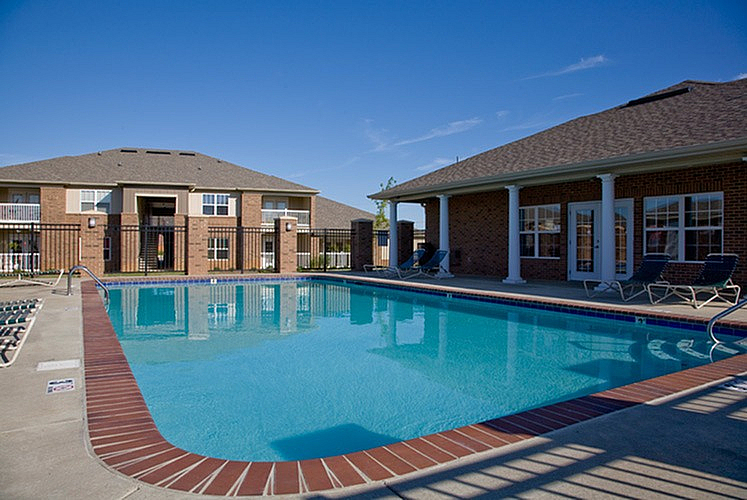 Inviting apartment community with a pristine swimming pool surrounded by well-maintained brick buildings and clear blue skies.