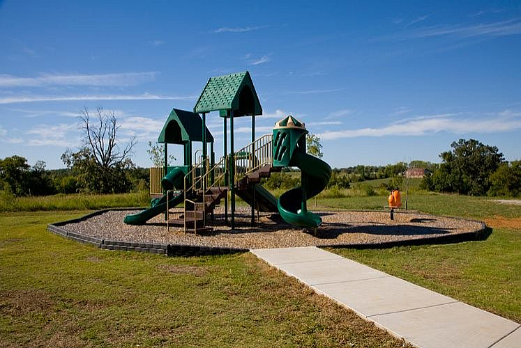 Inviting playground with vibrant green slides and climbing structures, set in a scenic park with a clear blue sky.