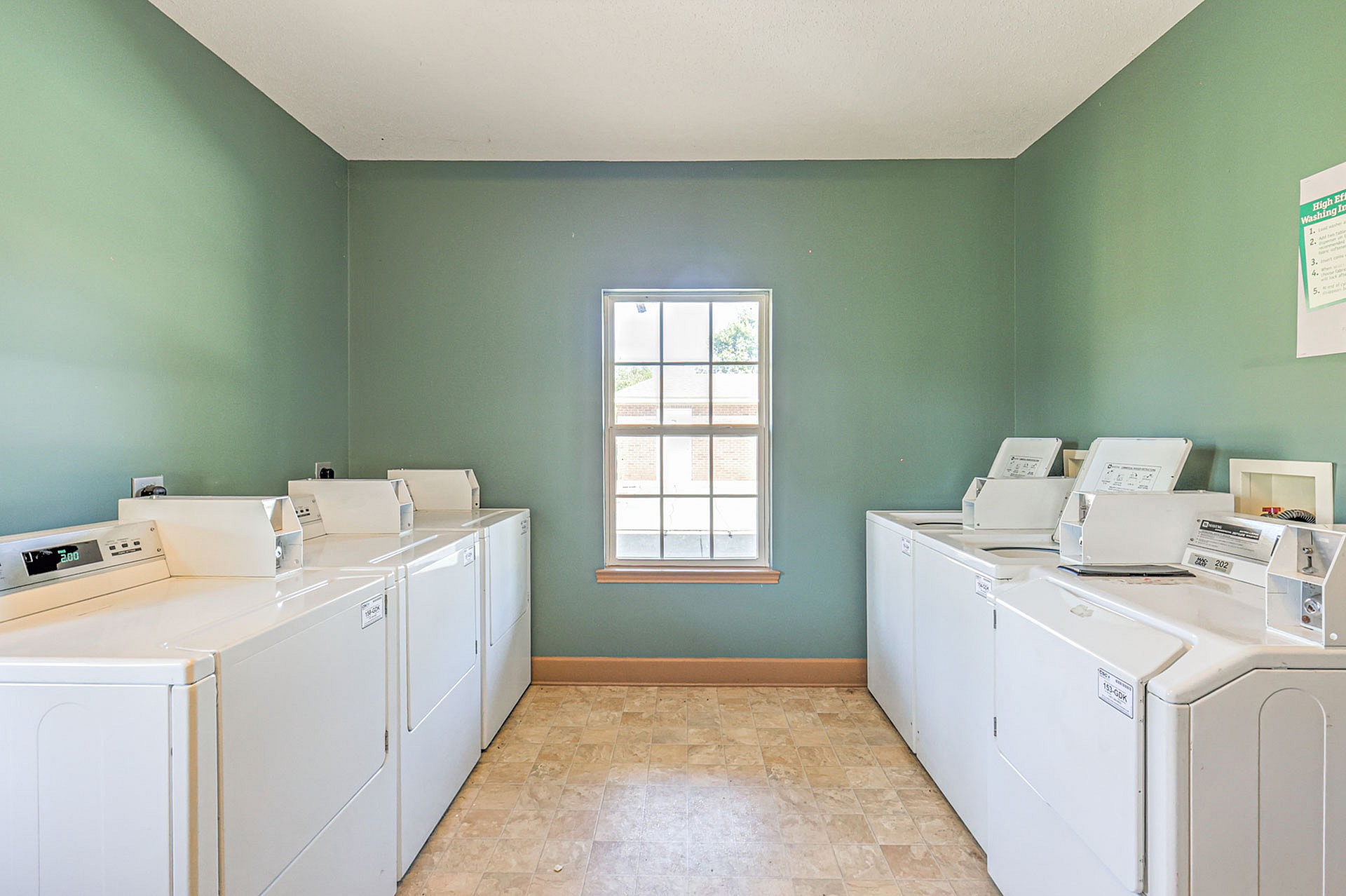 Bright and spacious laundry room with multiple modern washing machines and a large window, offering a cheerful and convenient laundry experience.