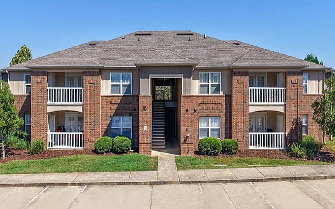 Charming two-story brick apartment building with white balconies, well-maintained landscaping, and inviting central entrance.