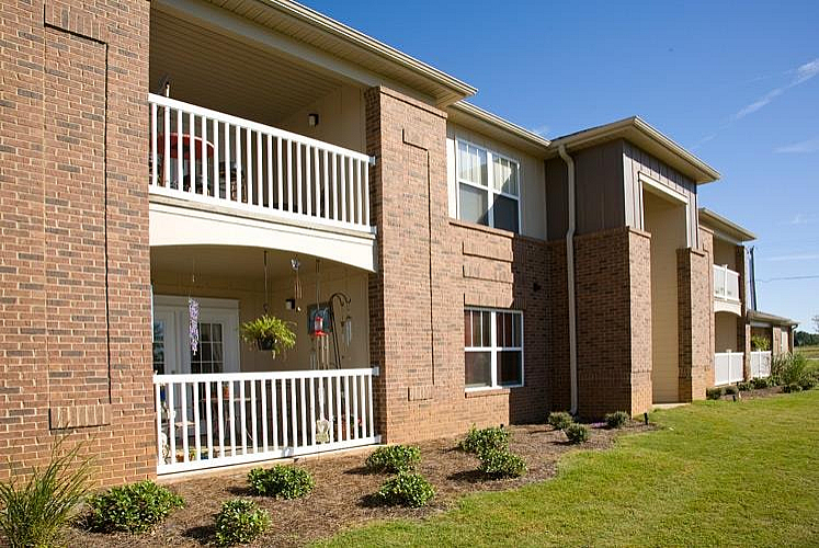 Charming apartment exterior with inviting balconies and well-maintained landscaping under a clear blue sky.