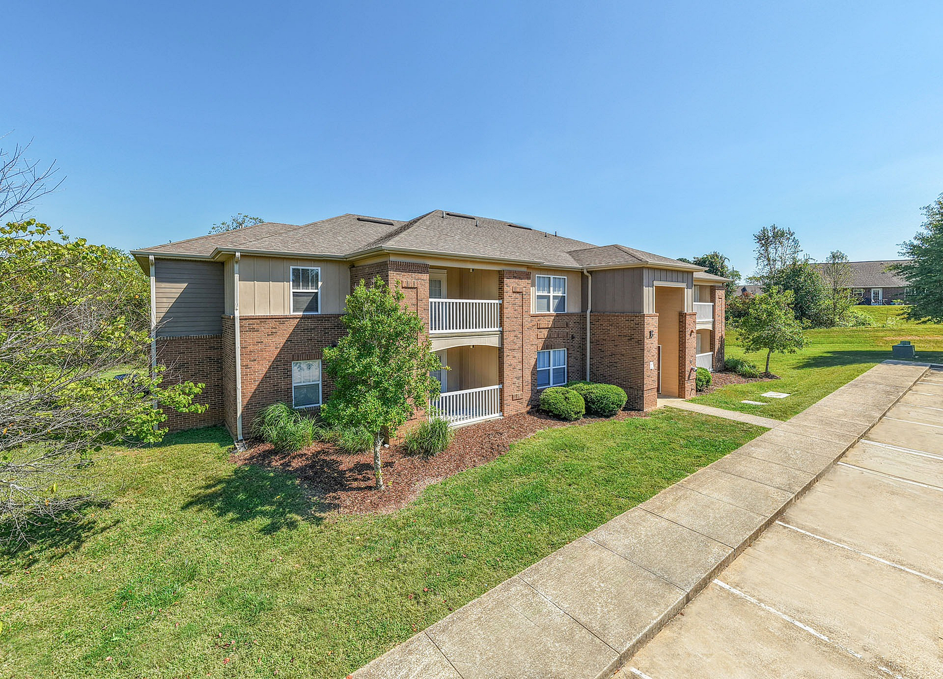 Charming two-story apartment building with brick exterior nestled in a lush green landscape, promising a serene and spacious living environment.
