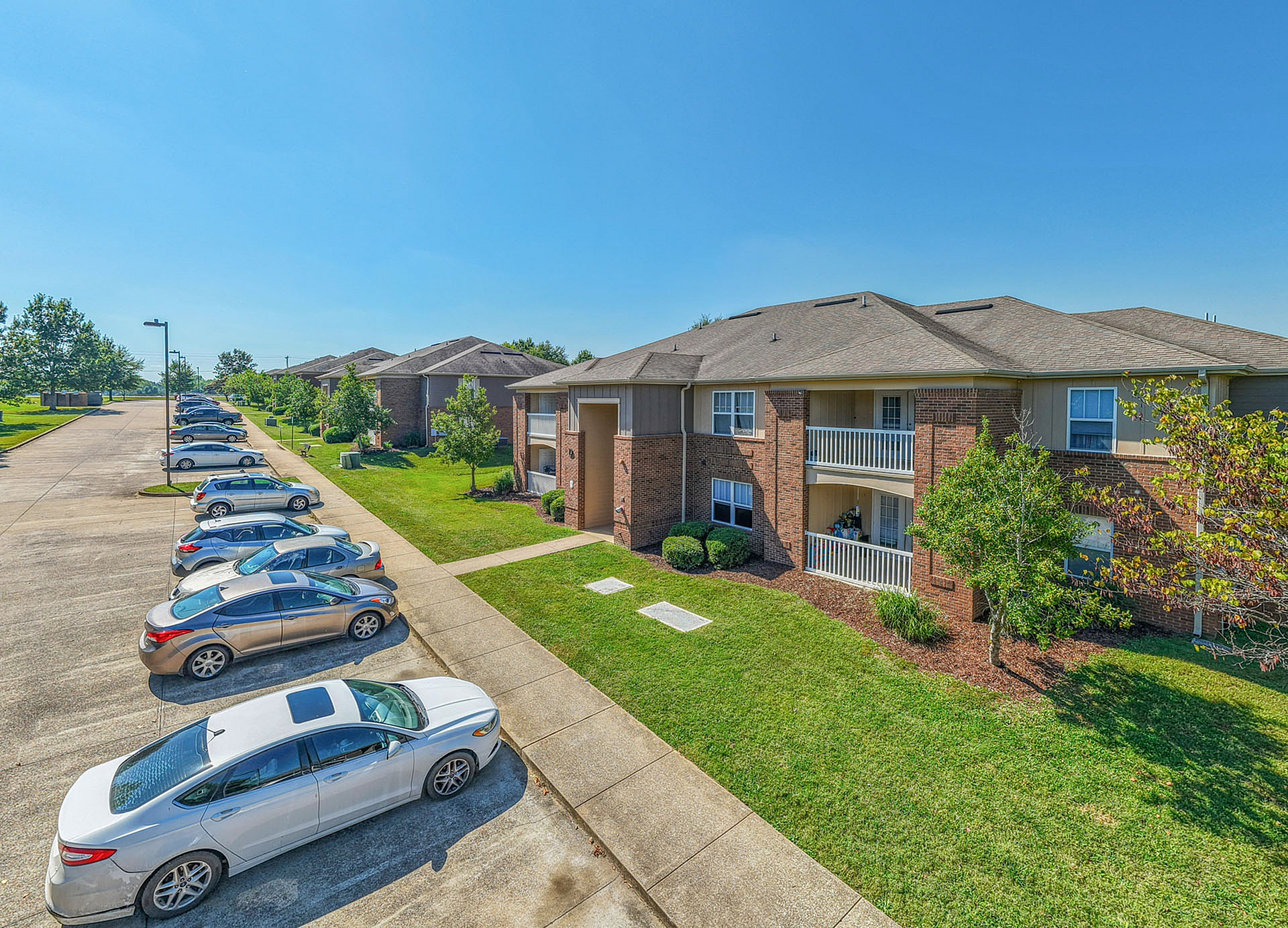 Charming apartment complex with elegant two-story brick buildings, inviting balconies, and well-maintained green spaces, all under a clear blue sky.