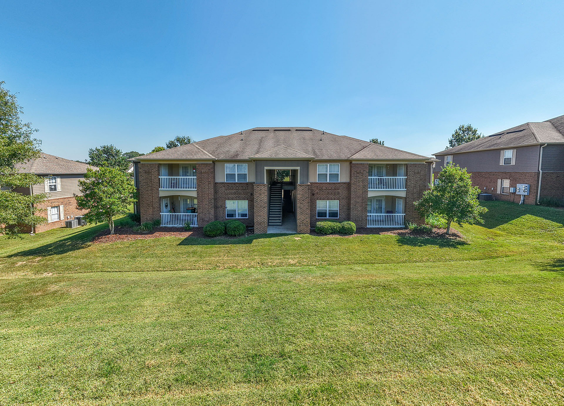 Charming brick apartment building with two levels, featuring inviting balconies and surrounded by lush green lawns.