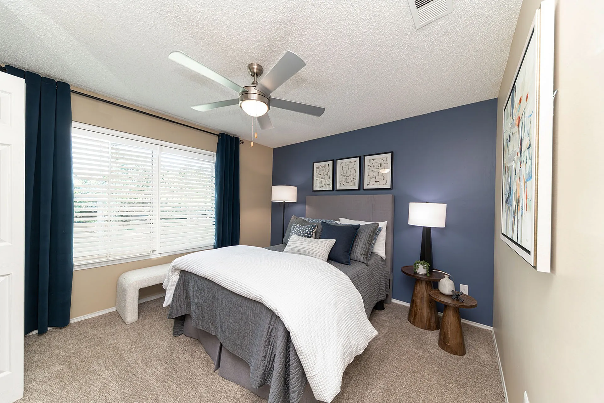 Cozy bedroom with elegant decor, featuring a plush bed, modern ceiling fan, and stylish side tables against a calming blue accent wall.