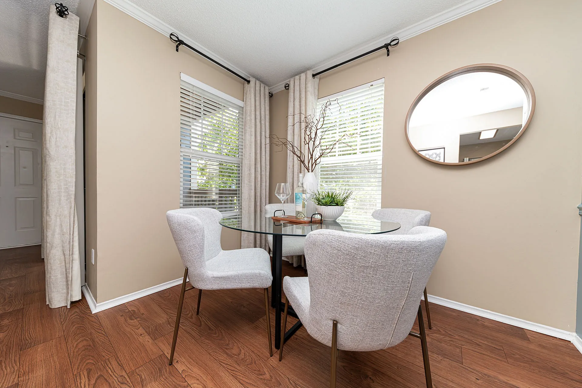 Elegant dining nook with a glass table and stylish chairs, enhanced by large windows and a modern wall mirror.