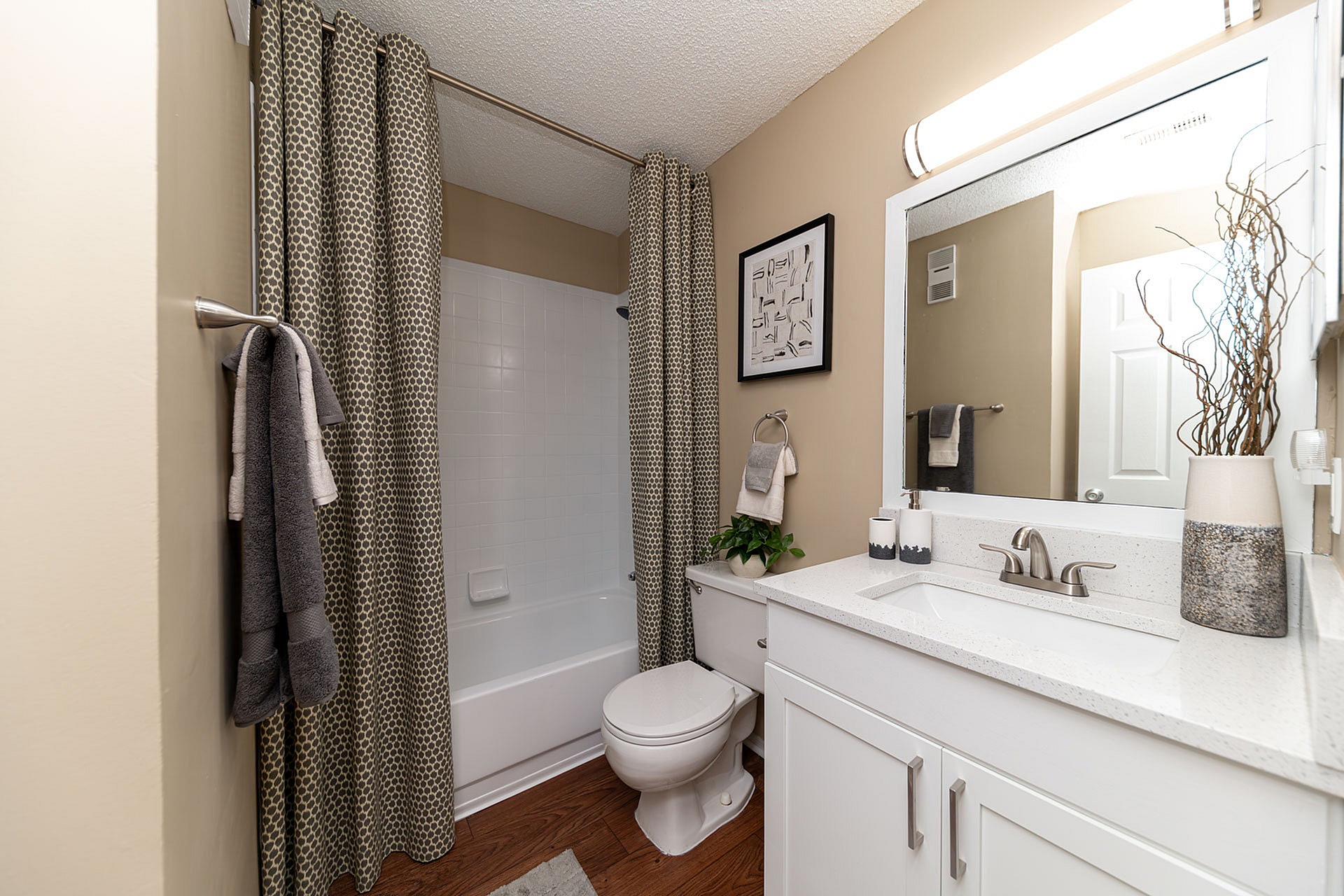 Modern bathroom featuring elegant design with a white vanity, sleek faucet, and stylish decor. Cozy bathtub with patterned shower curtain and fresh greenery adds a soothing touch.