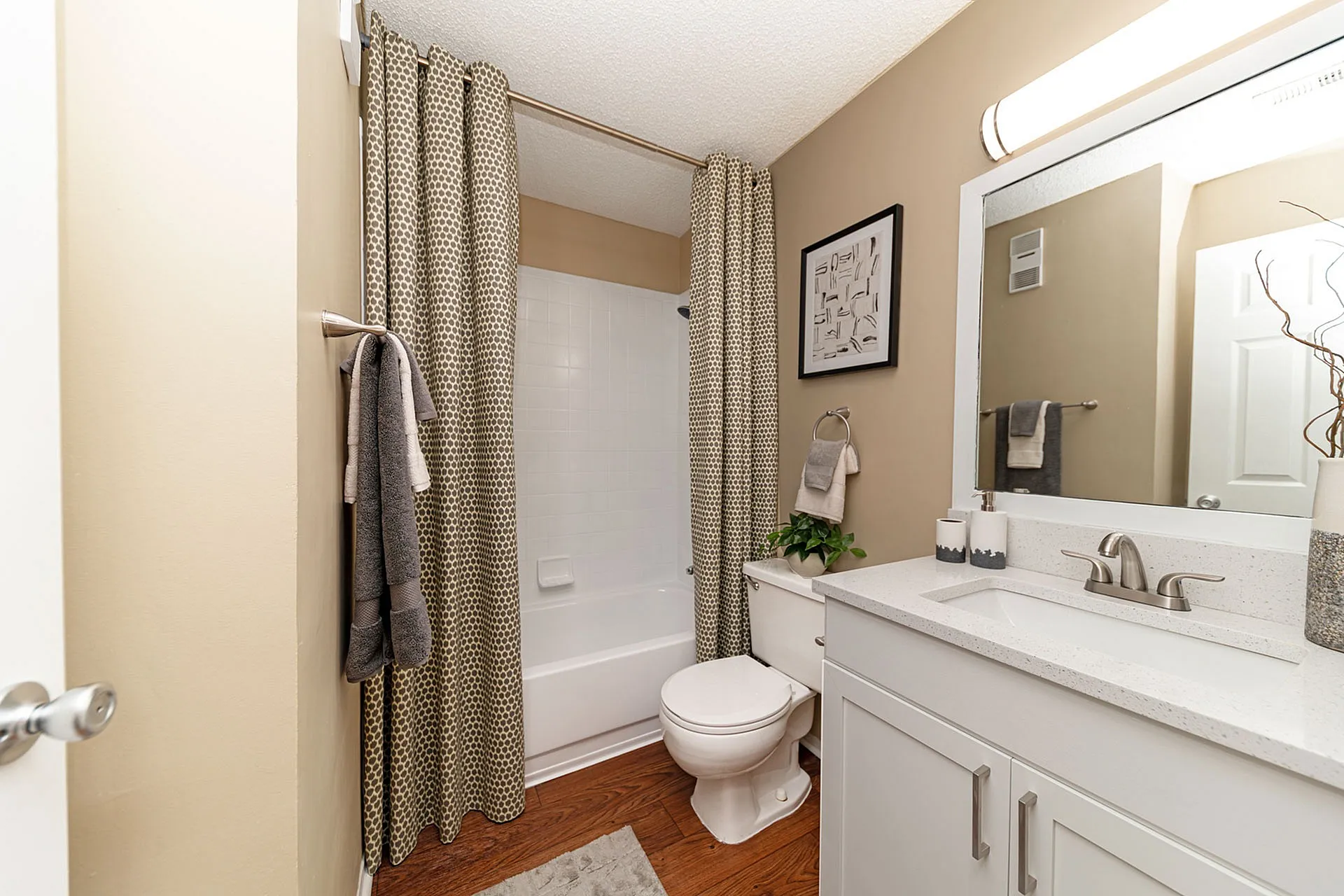 Elegant bathroom with modern vanity, stylish patterned shower curtain, and warm wood flooring for a cozy ambiance.