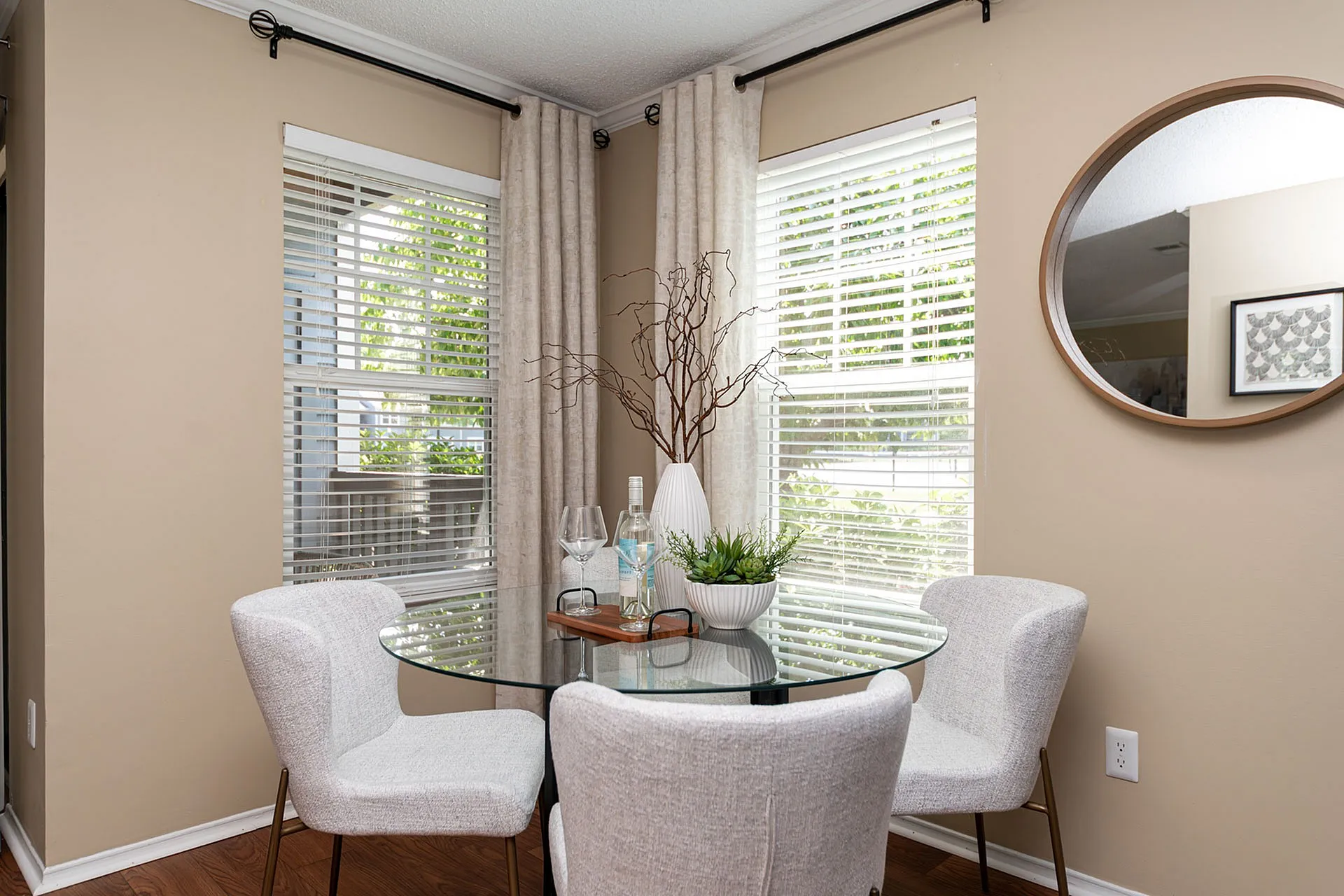 Chic dining nook with glass table, elegant decor, and natural light through tinted windows.