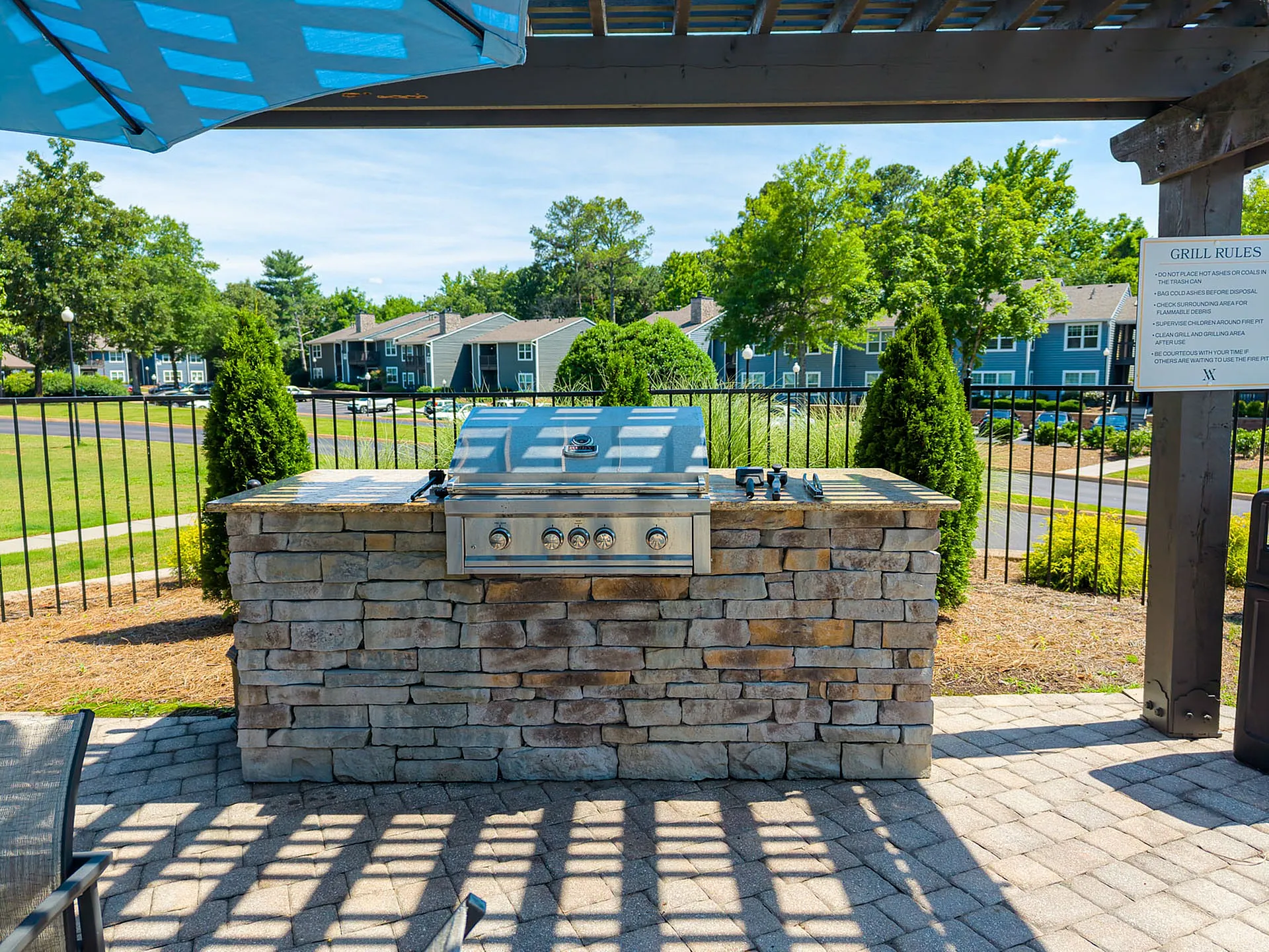 Inviting outdoor barbecue area with a stylish stone grill station under a charming pergola, surrounded by lush green landscaping.