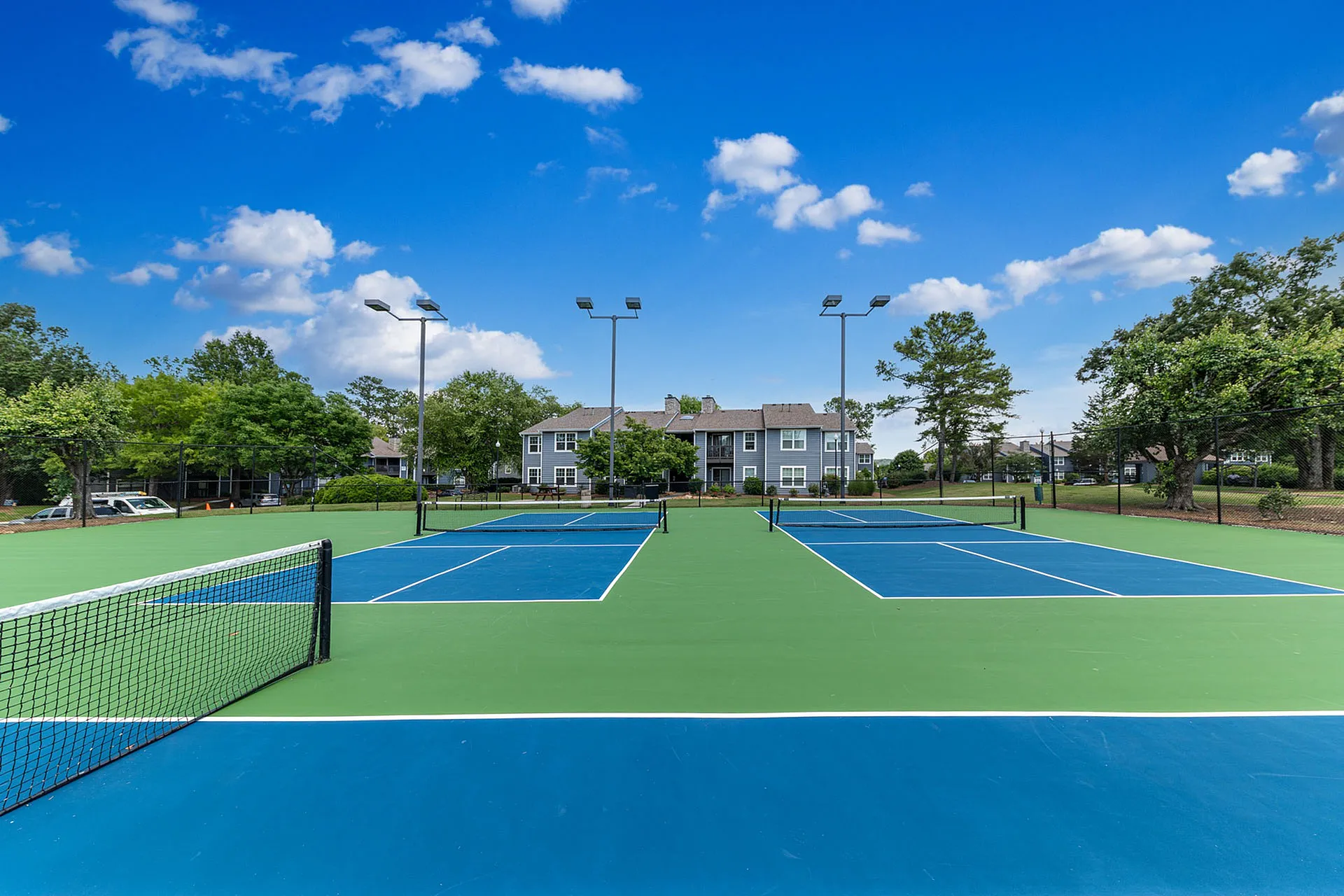 Vibrant tennis courts with lush greenery and modern apartment buildings in the background, under a clear blue sky.