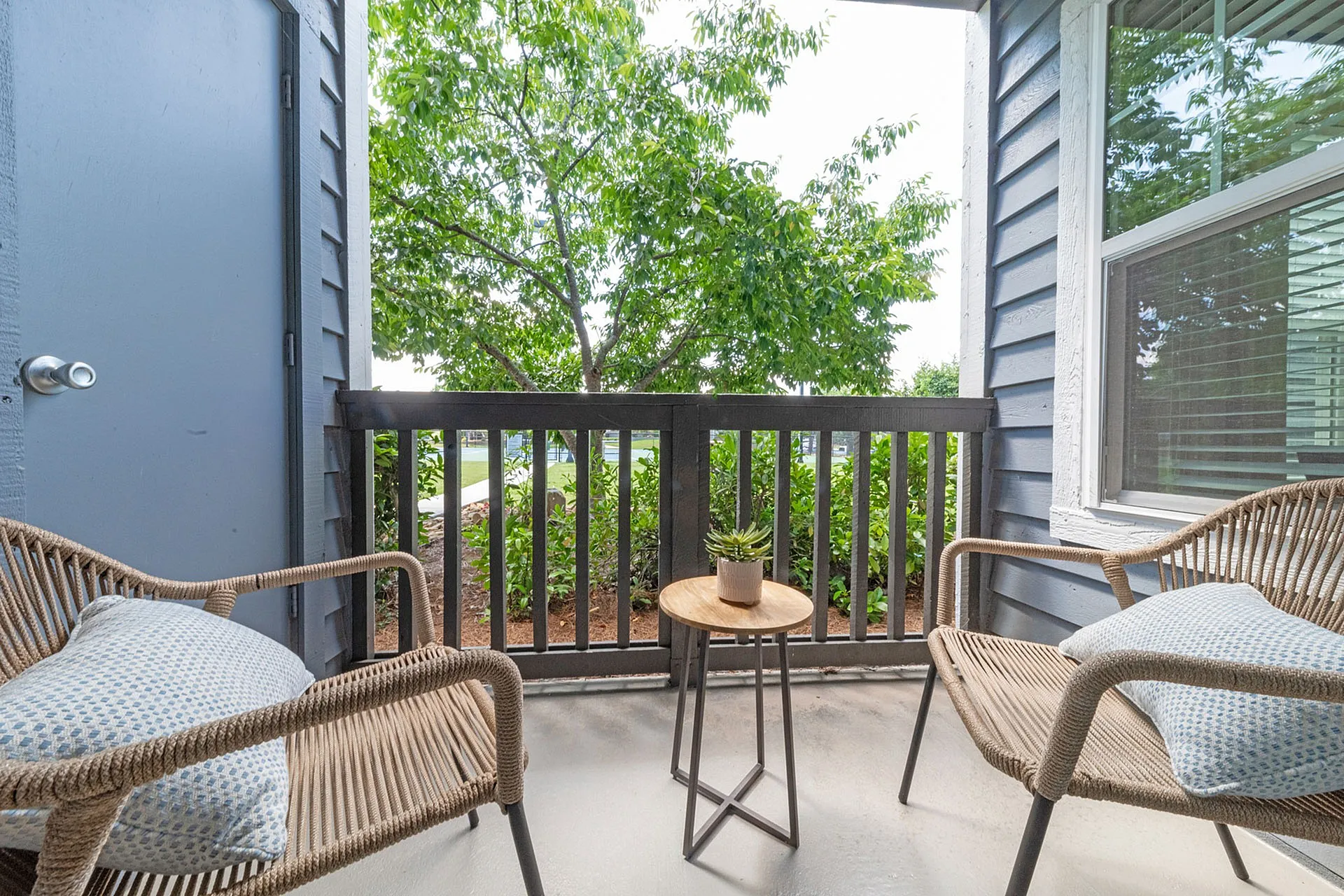 Charming apartment balcony with cozy seating, overlooking lush greenery and offering a peaceful retreat.