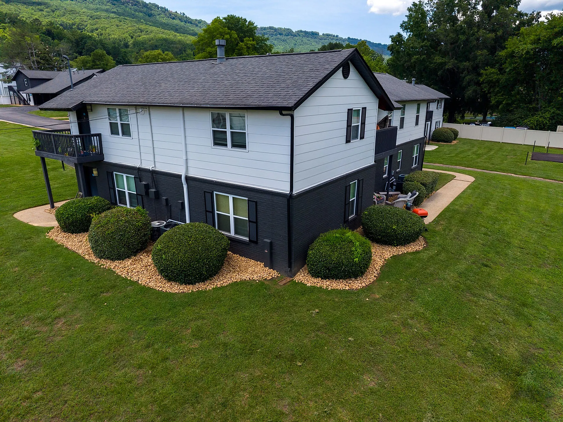 Charming two-story apartment building with stylish black and white exterior, nestled in lush greenery with scenic mountain views.