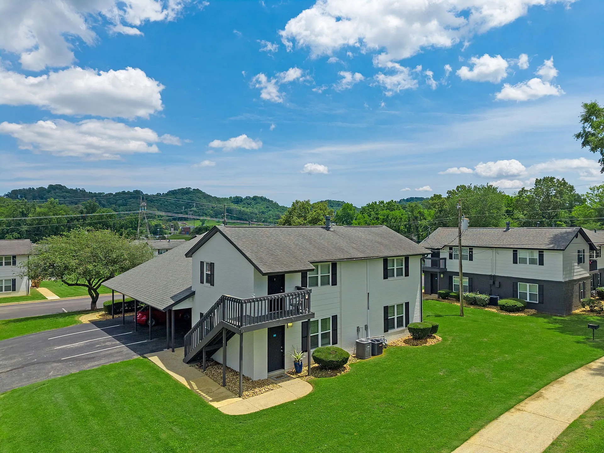 Charming apartment complex with lush green lawns, set against serene mountain views under a bright blue sky.