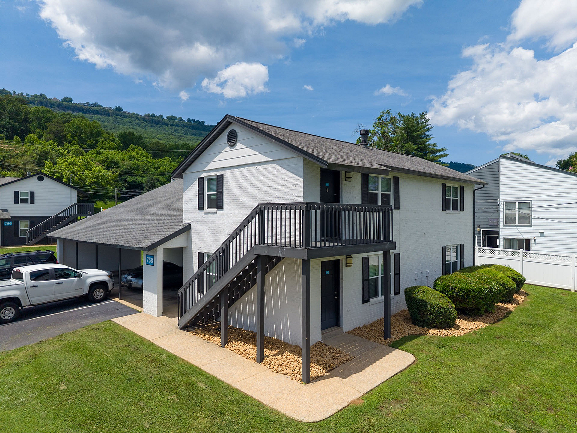 Charming two-story apartment building with private entrances, surrounded by lush greenery and scenic mountain views.