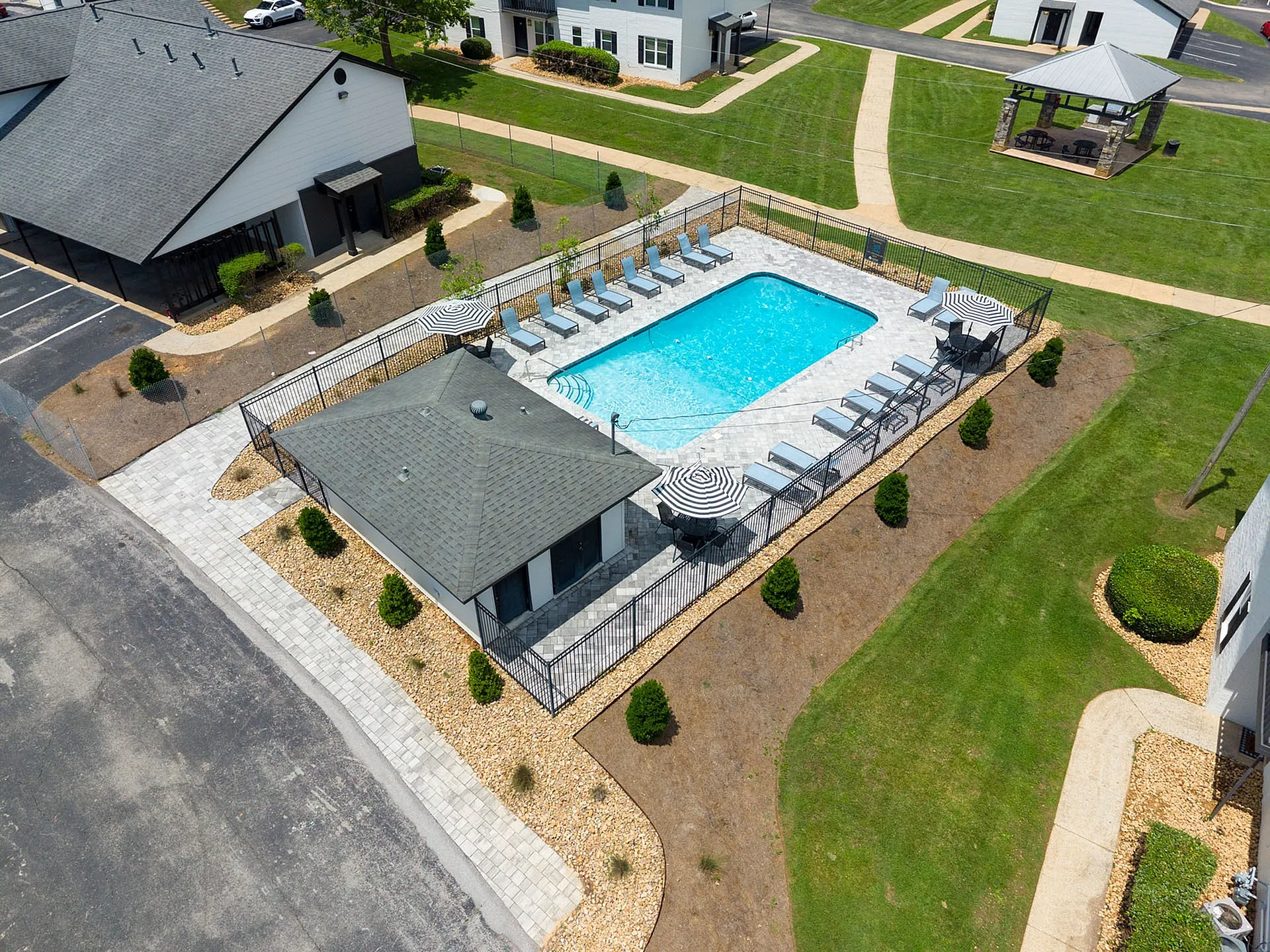 Elegant aerial view of a pristine swimming pool surrounded by stylish lounge chairs and chic umbrellas, set in a lush green community space.