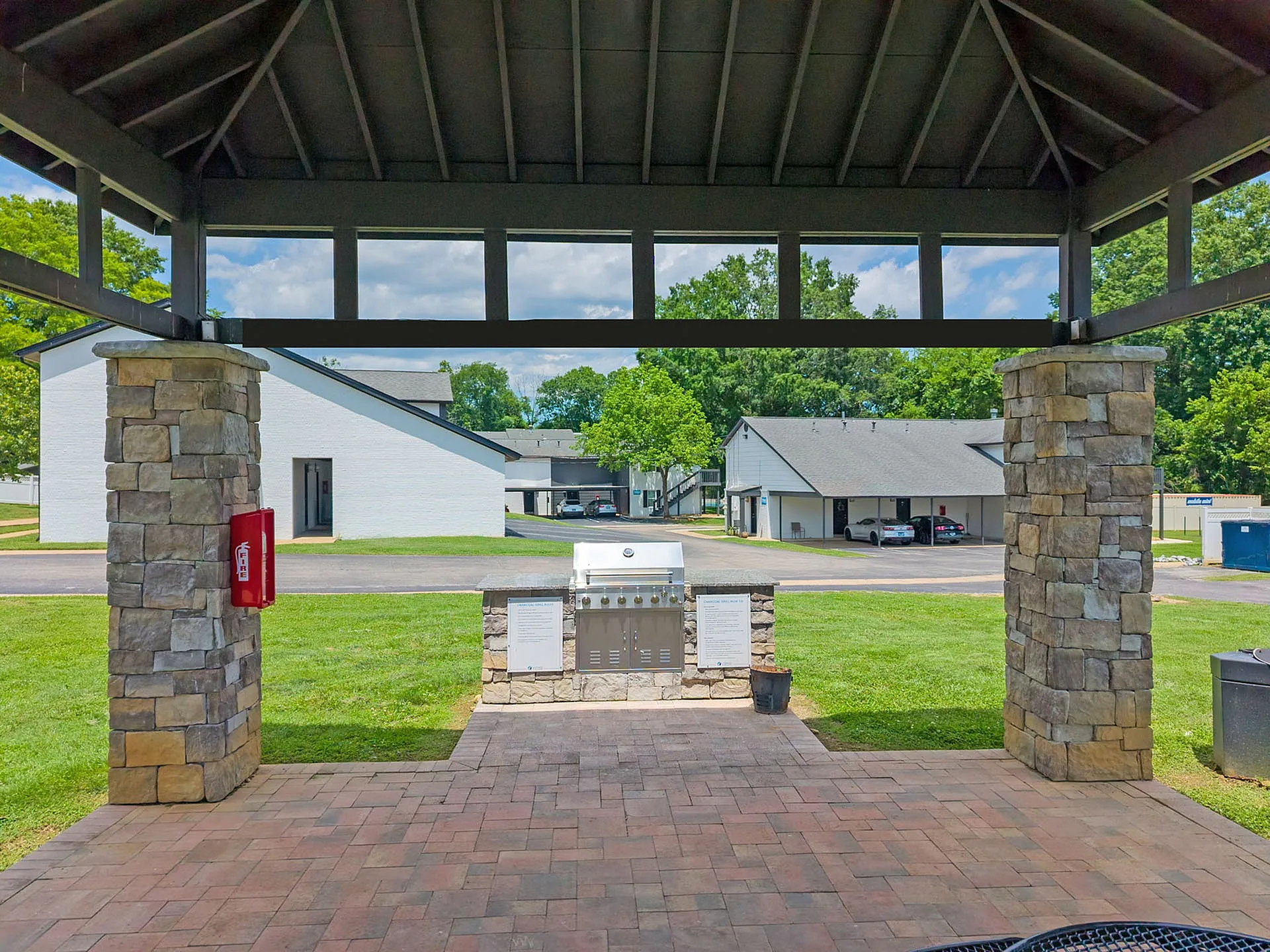 Charming outdoor view featuring a covered pavilion with stone pillars, stylish outdoor grill, and vibrant communal area with lush greenery.
