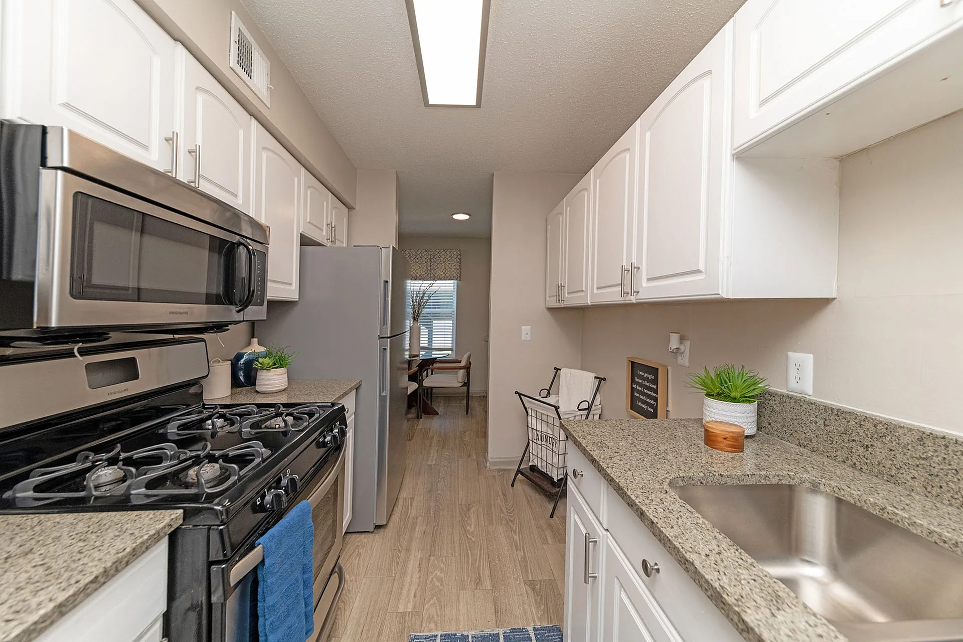 Modern kitchen with sleek stainless steel appliances, elegant granite countertops, and stylish white cabinetry leading to a cozy dining area.