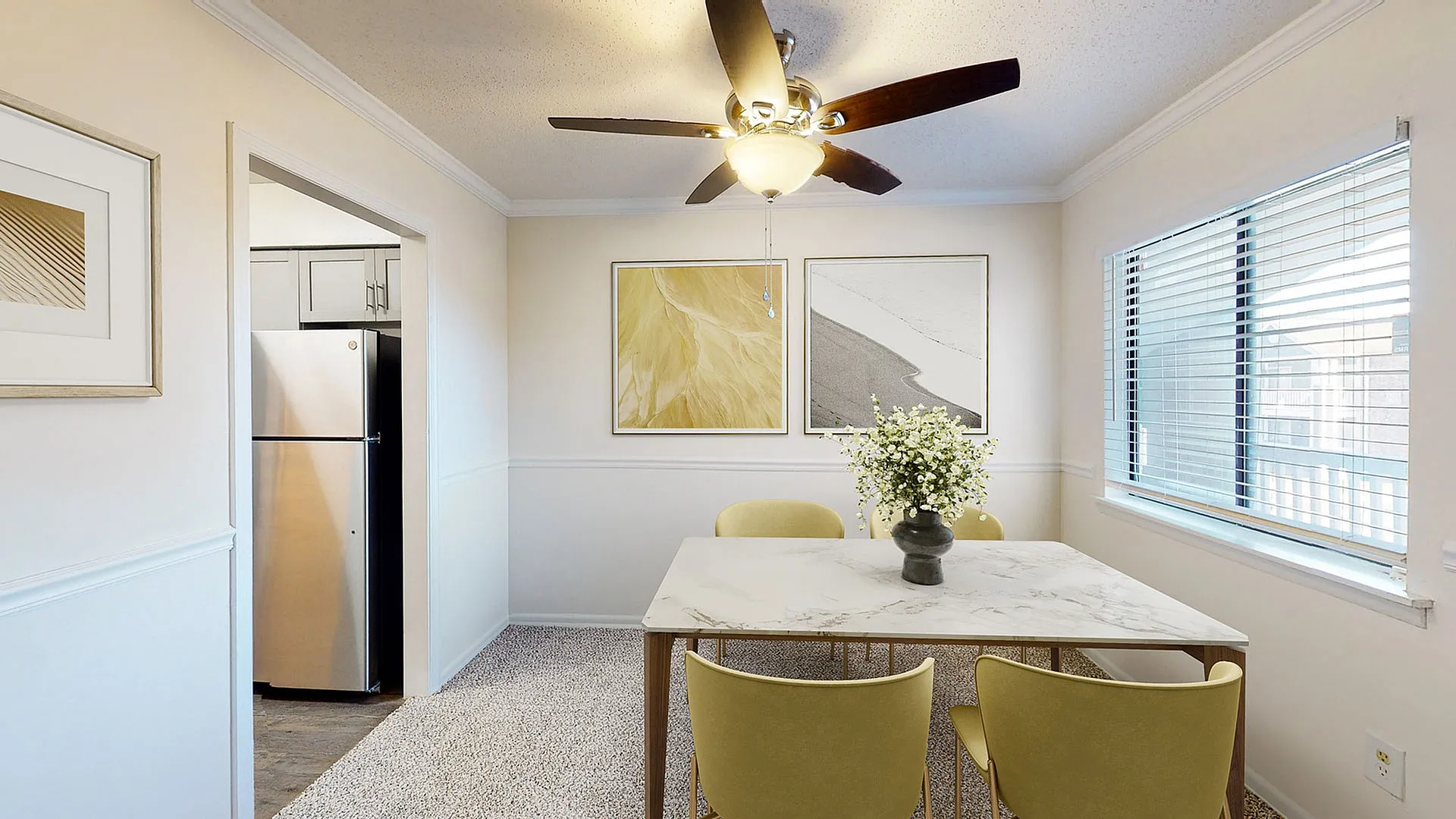 Bright dining area with a modern marble table, elegant ceiling fan, vibrant artwork, and natural light streaming through large windows.