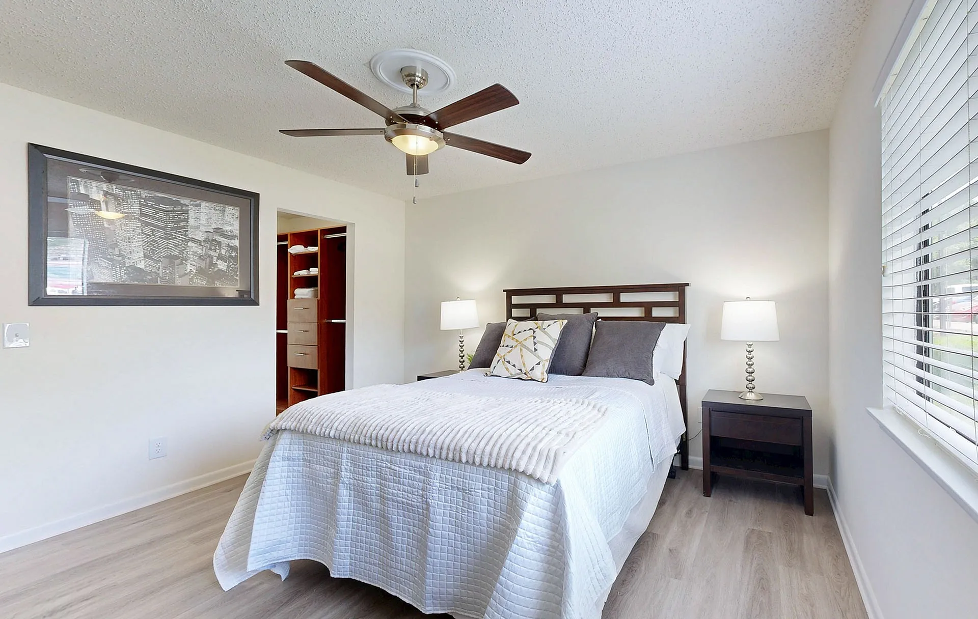 Bright and inviting bedroom with modern ceiling fan, plush bedding, and spacious closet, complemented by natural light from a large window.