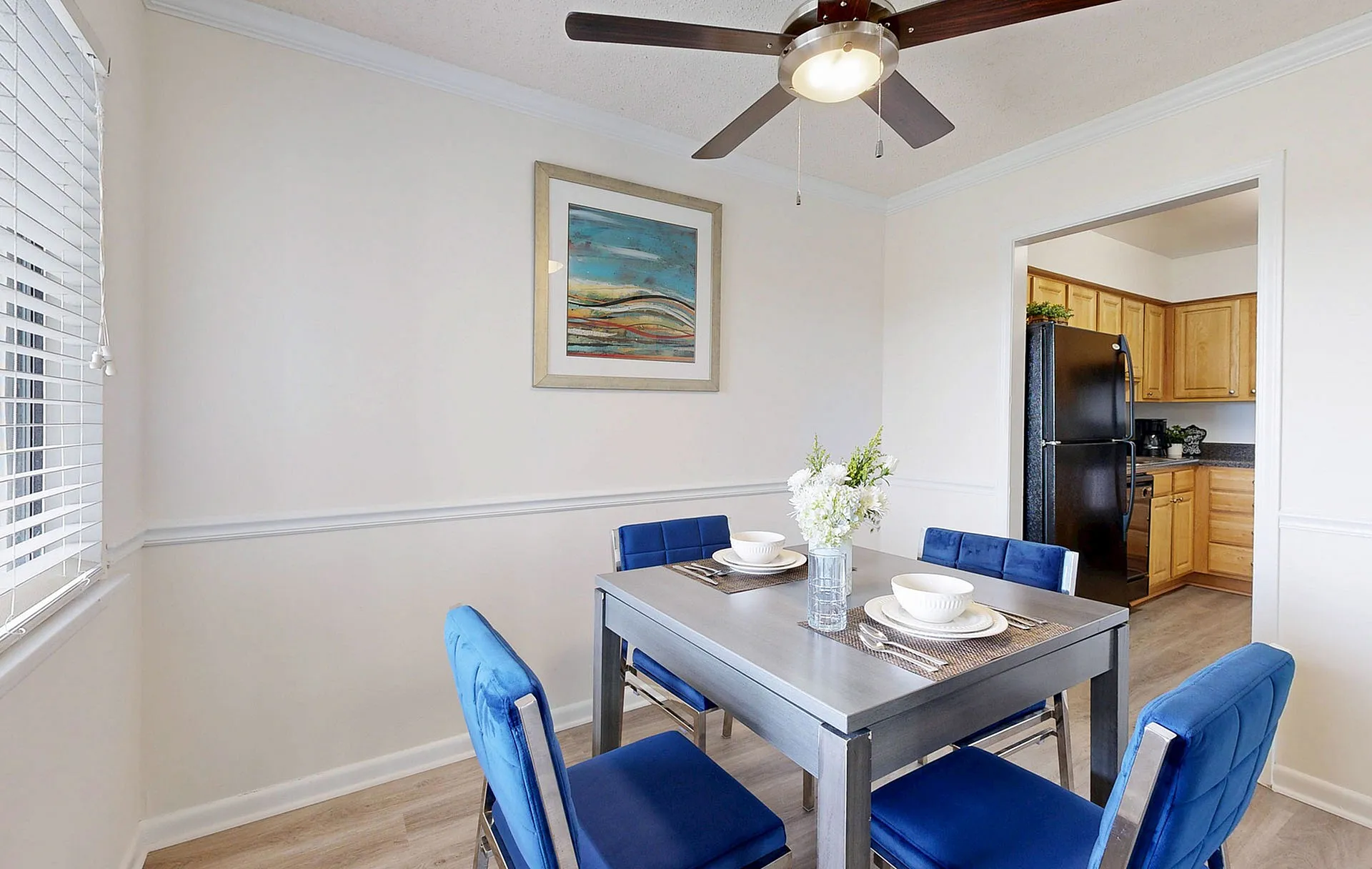 Charming dining area with modern table, stylish blue chairs, and bright decor opening into a warm wooden kitchen.