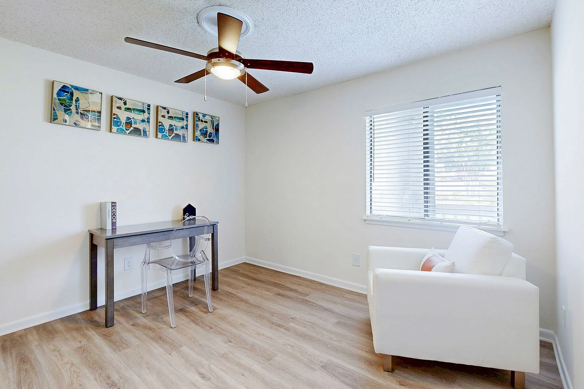 Bright and modern home office with elegant wood flooring, a sleek desk, acrylic chair, and cozy white armchair, perfect for productivity and relaxation.