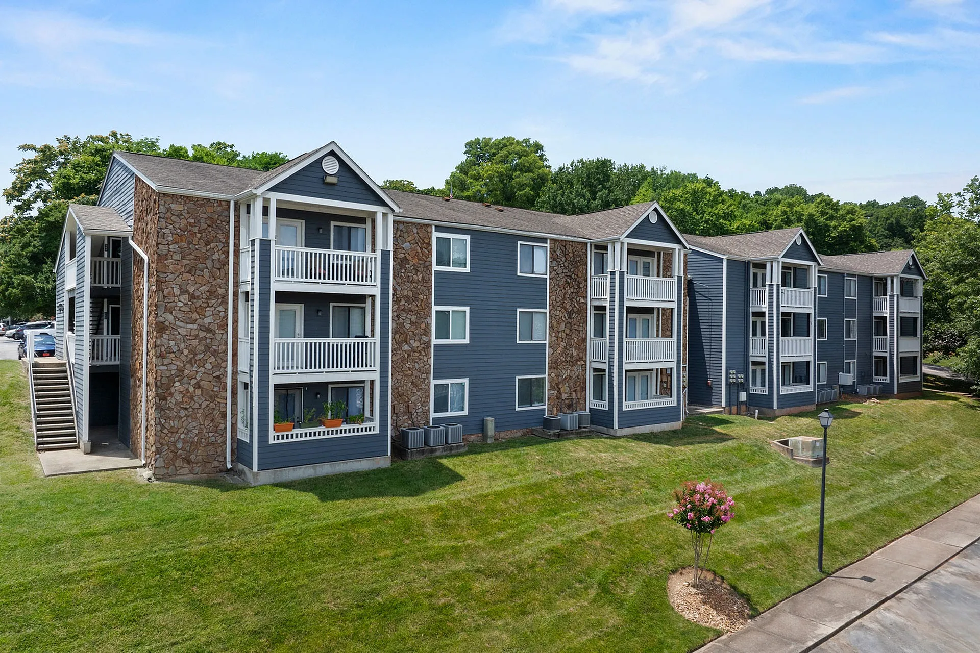 Charming multi-story apartment complex with stone accents and lush green surroundings, offering serene living spaces and private balconies.
