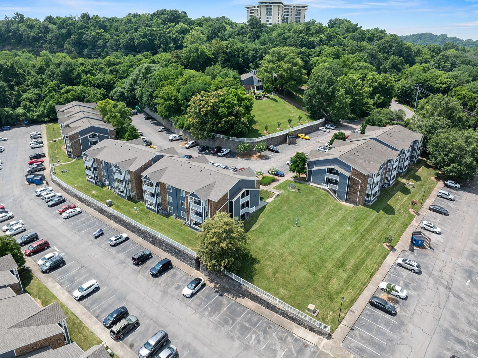 Aerial view of a picturesque apartment complex surrounded by lush greenery, featuring modern architecture and ample parking space.
