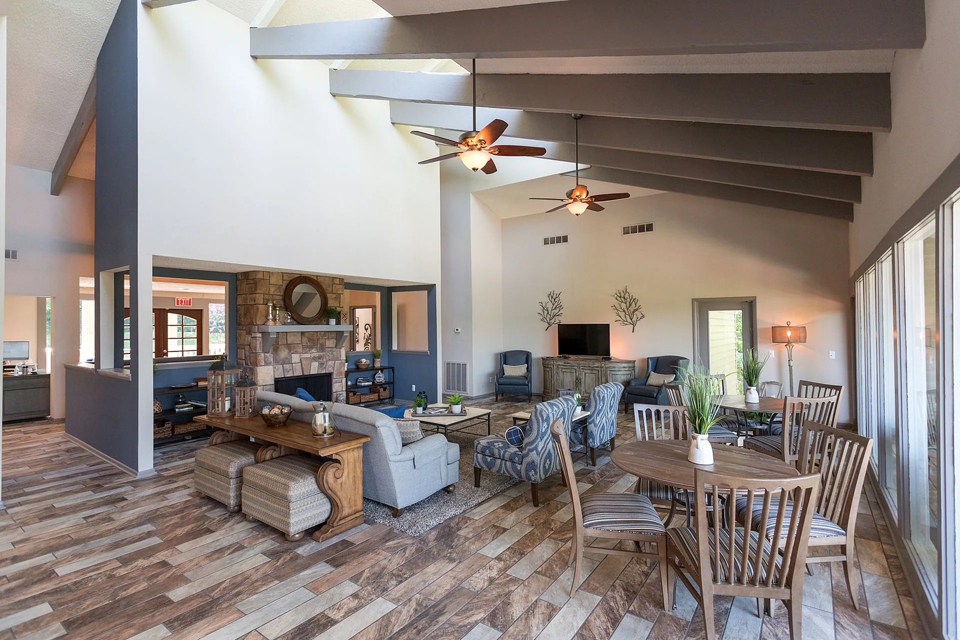 Inviting living room with high vaulted ceilings, modern ceiling fans, and expansive windows, featuring stylish seating, a cozy stone fireplace, and elegant dining area.