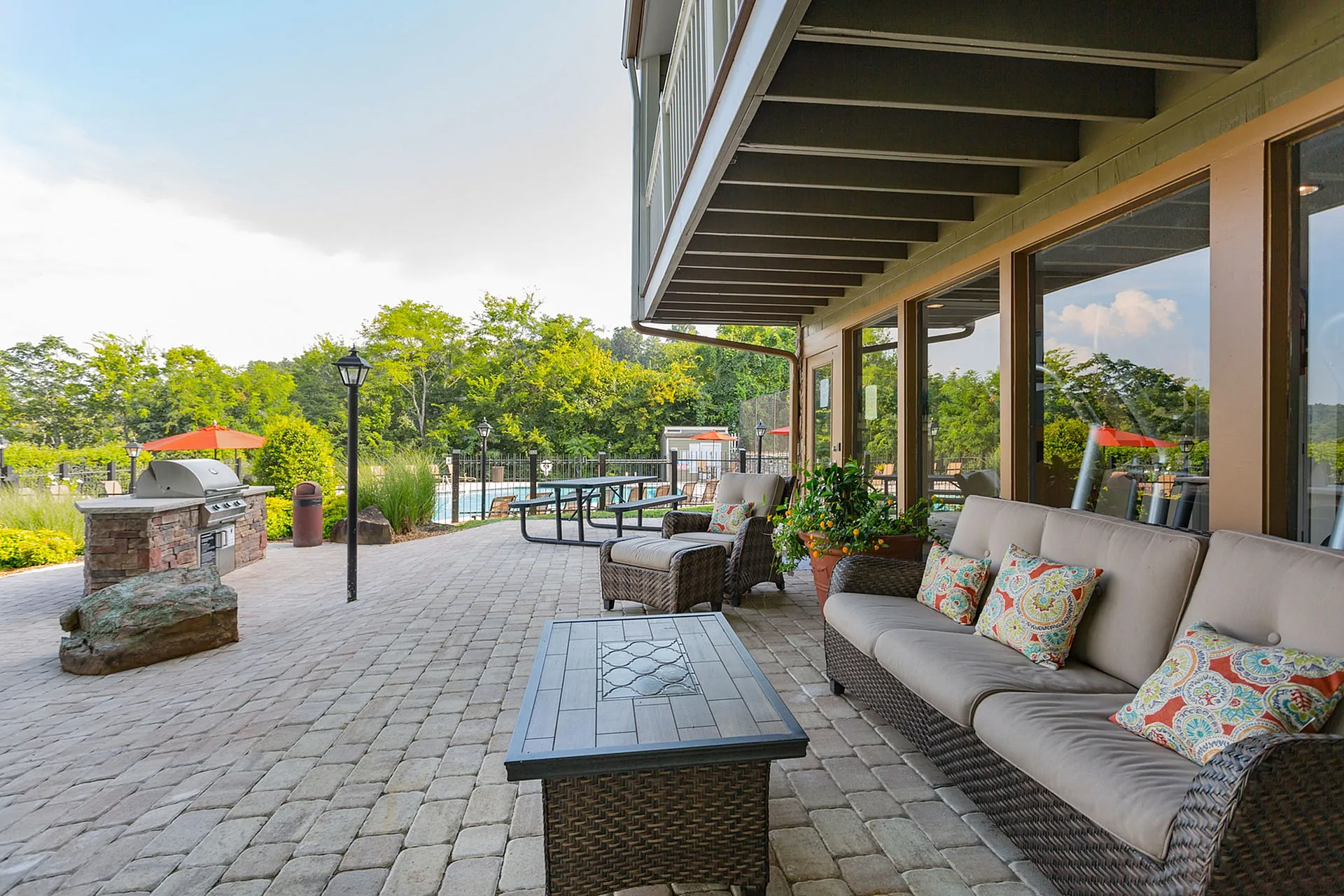 Inviting outdoor patio with elegant wicker seating, vibrant cushions, and a stylish grill area overlooking a lush garden and pool.