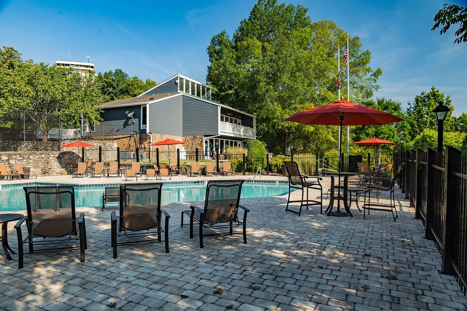 Luxurious outdoor pool area with stylish lounge chairs, red patio umbrellas, and lush greenery creating a serene retreat.