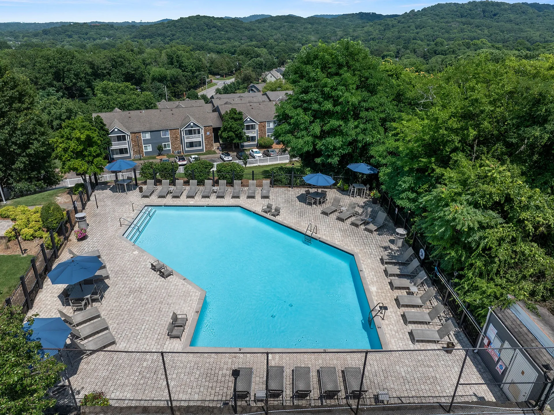 Inviting outdoor pool area with comfortable lounge chairs and umbrellas, surrounded by lush greenery and residential buildings in a serene setting.