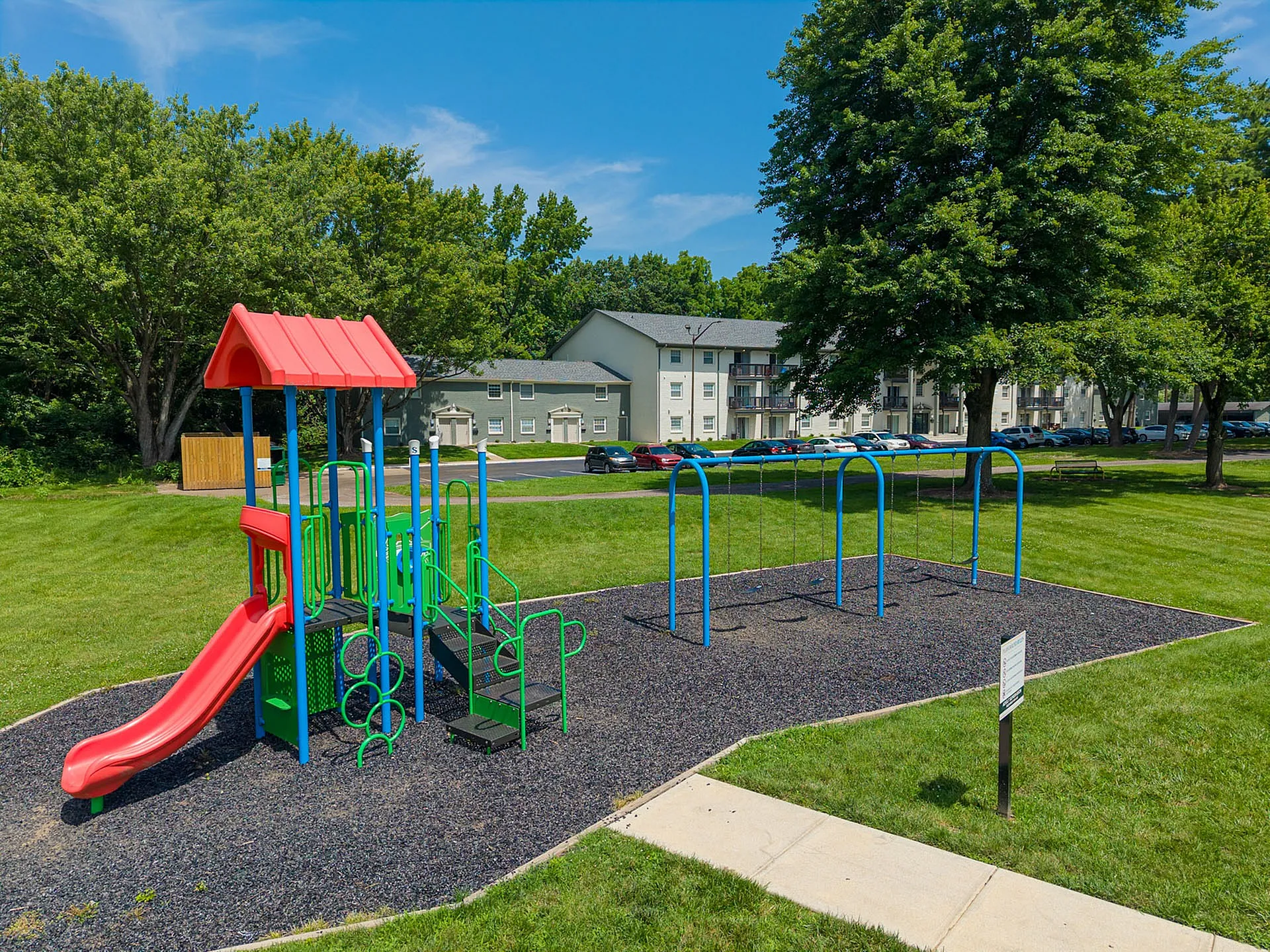 Inviting playground with vibrant slides and swings, surrounded by lush greenery and modern apartment buildings.