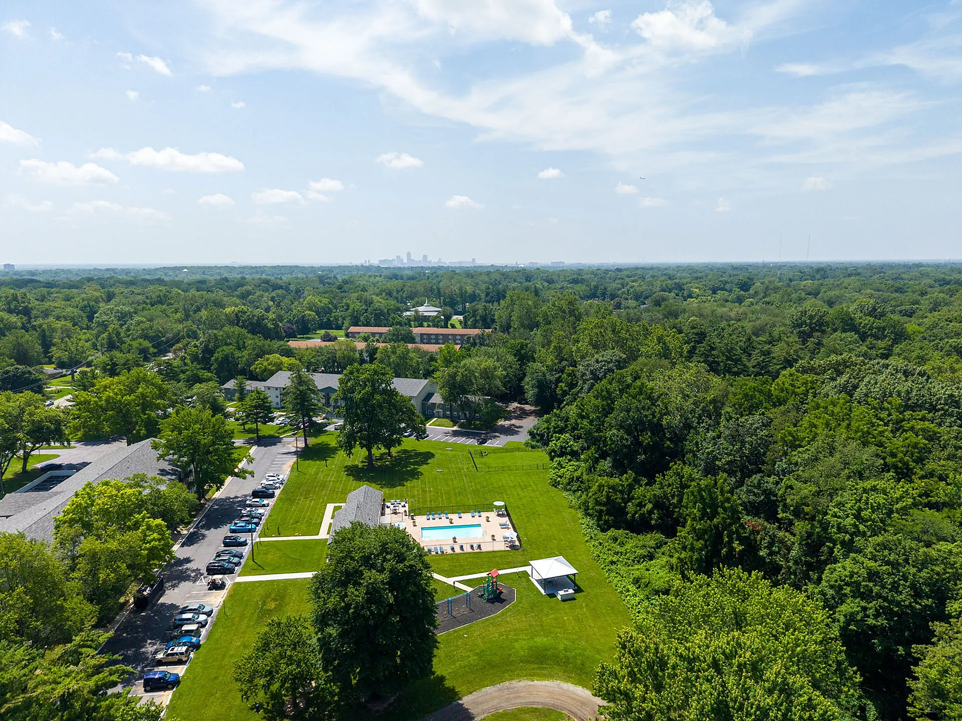 Stunning aerial view of a tranquil apartment community nestled in lush greenery, featuring a sparkling swimming pool and a welcoming picnic area.