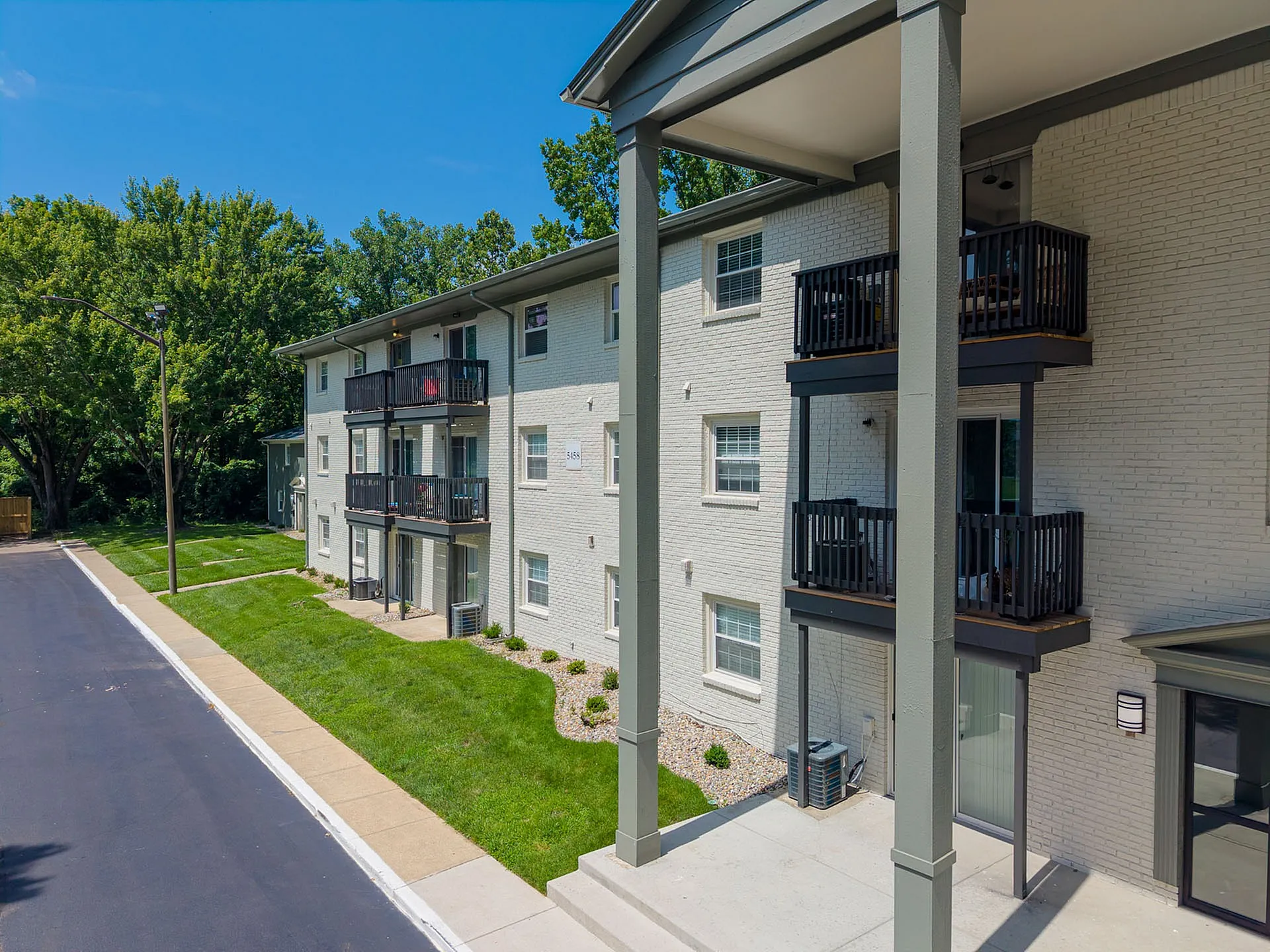 Charming three-story apartment building with elegant balconies, surrounded by lush greenery and modern landscaping.