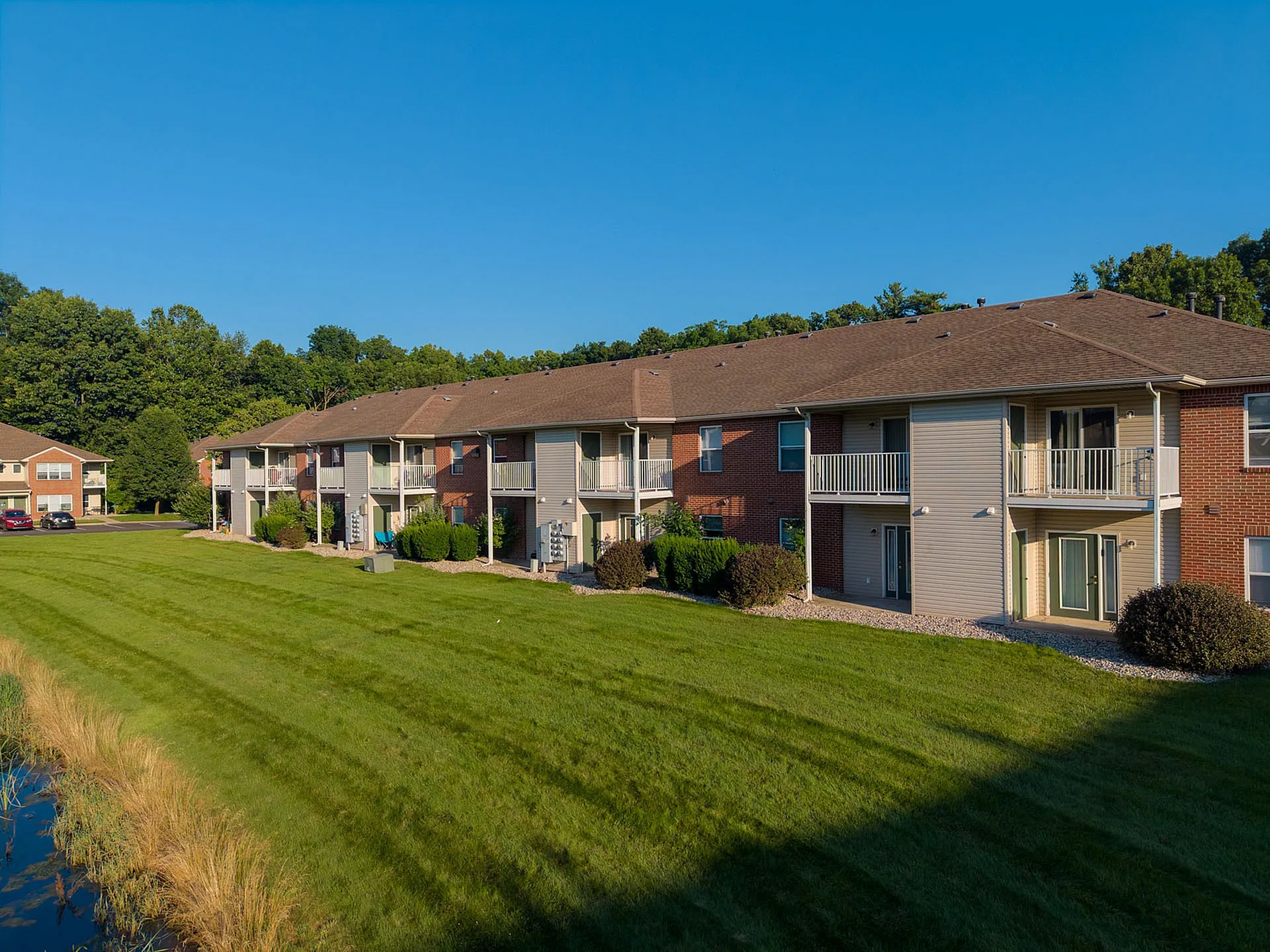 Charming apartment complex with private balconies and lush green landscaping under a clear blue sky.
