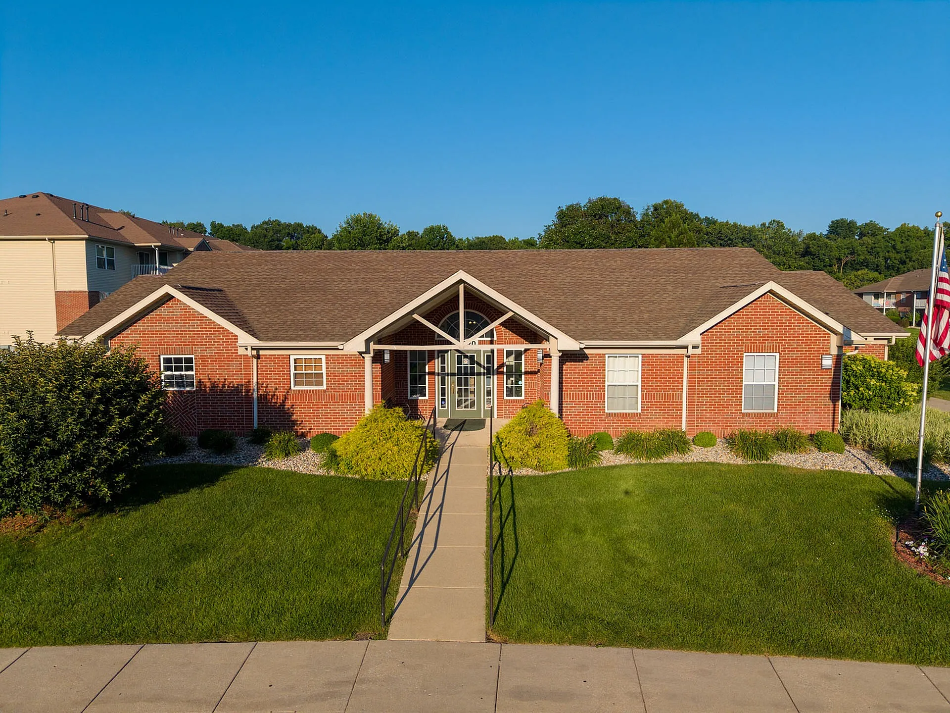 Beautiful brick community center with manicured lawn, outdoor walkway, and bright entryway under clear blue skies.
