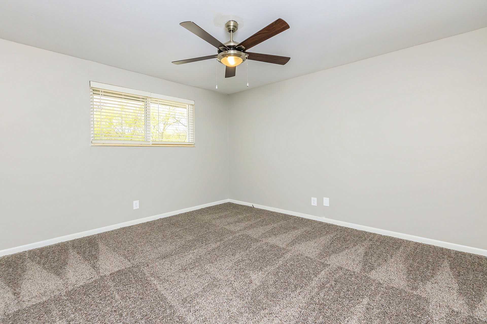 Spacious empty room with plush carpet and modern ceiling fan, ready for personalized touches.