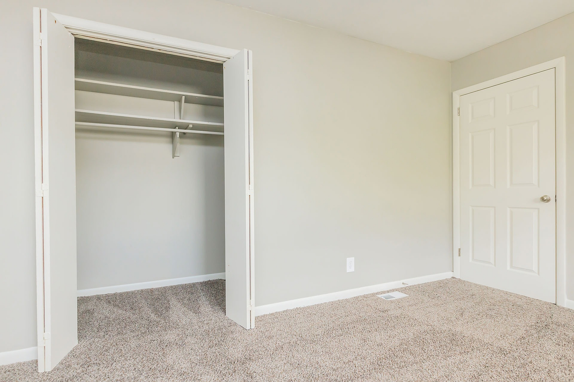 Bright and airy room with plush carpeting, open closet space, and elegant neutral tones.