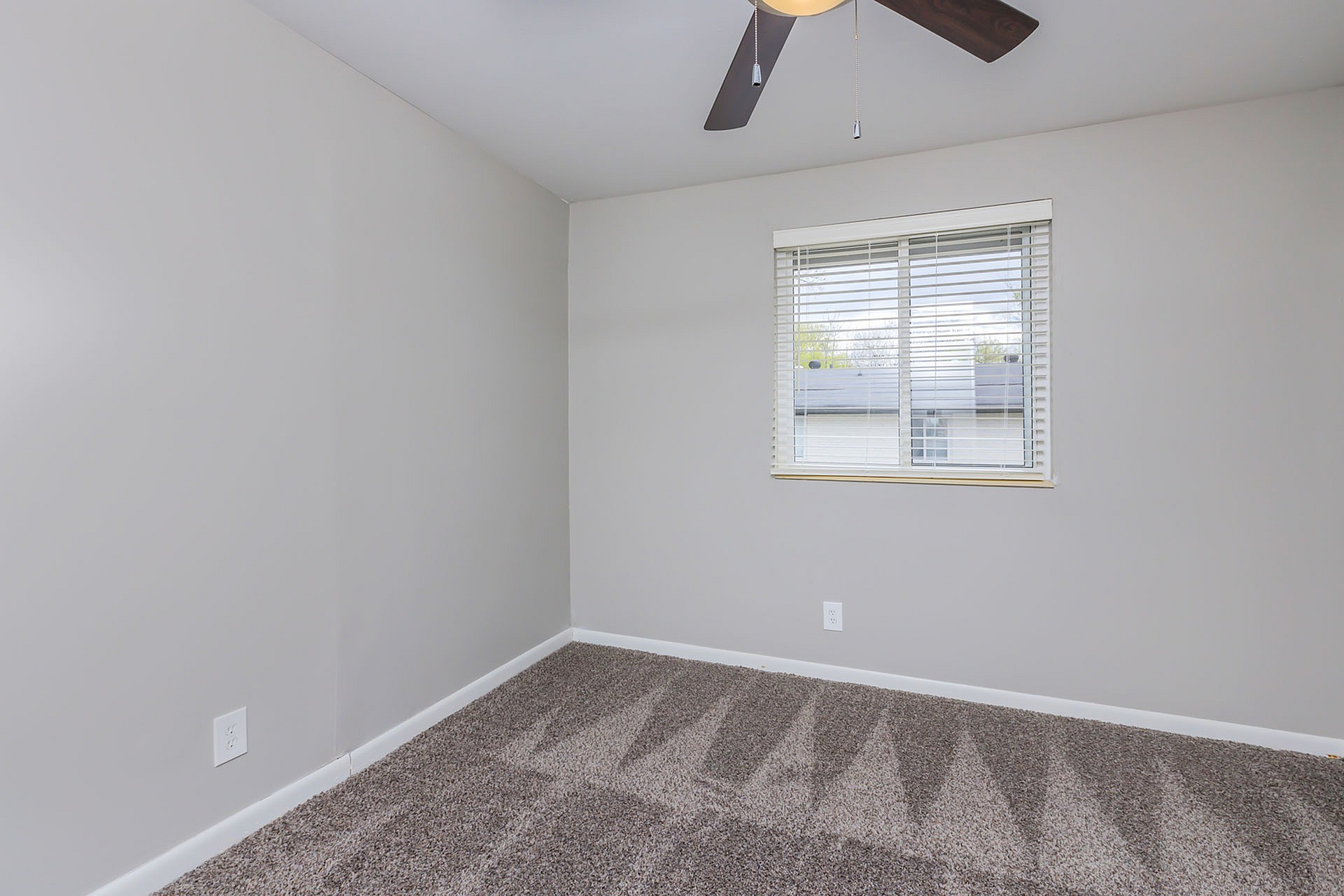 Bright and airy room with plush carpeting and a large window offering natural light, perfect for a cozy bedroom or home office.