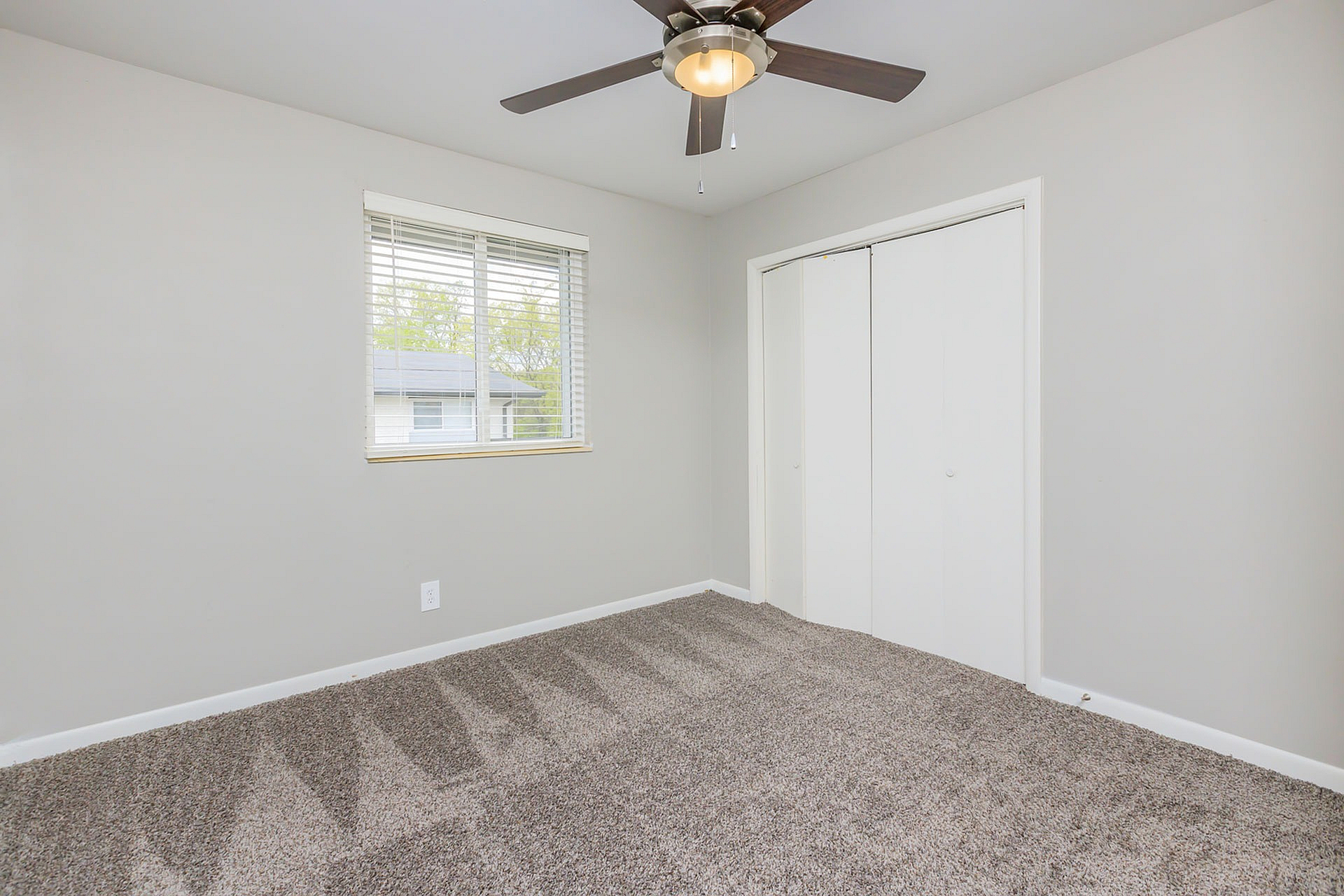 Bright and airy empty room with plush carpeting, modern ceiling fan, and a large window for plenty of natural light.