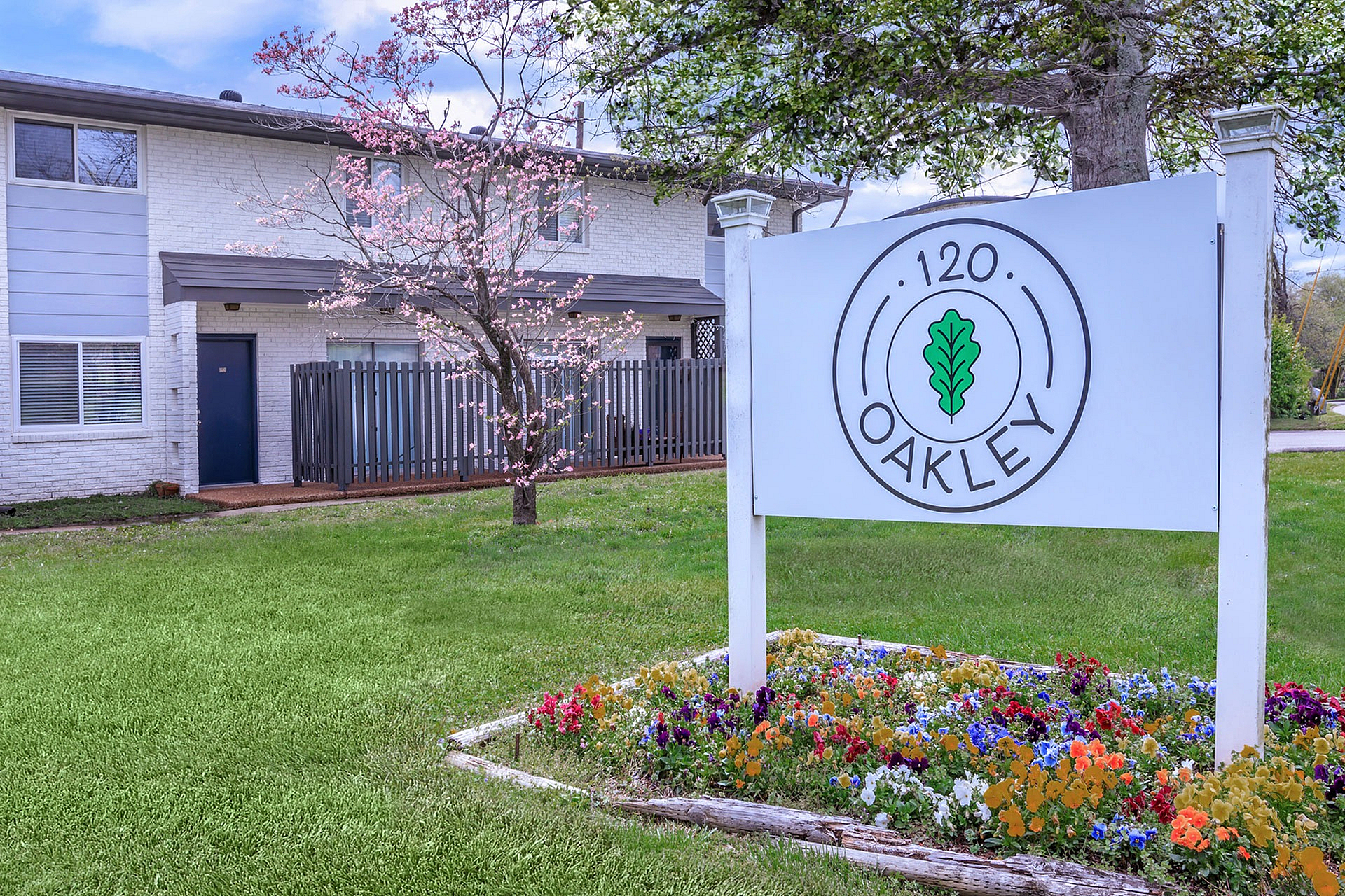 Charming apartment community at 120 Oakley, featuring vibrant landscaping and a welcoming exterior with blooming trees.