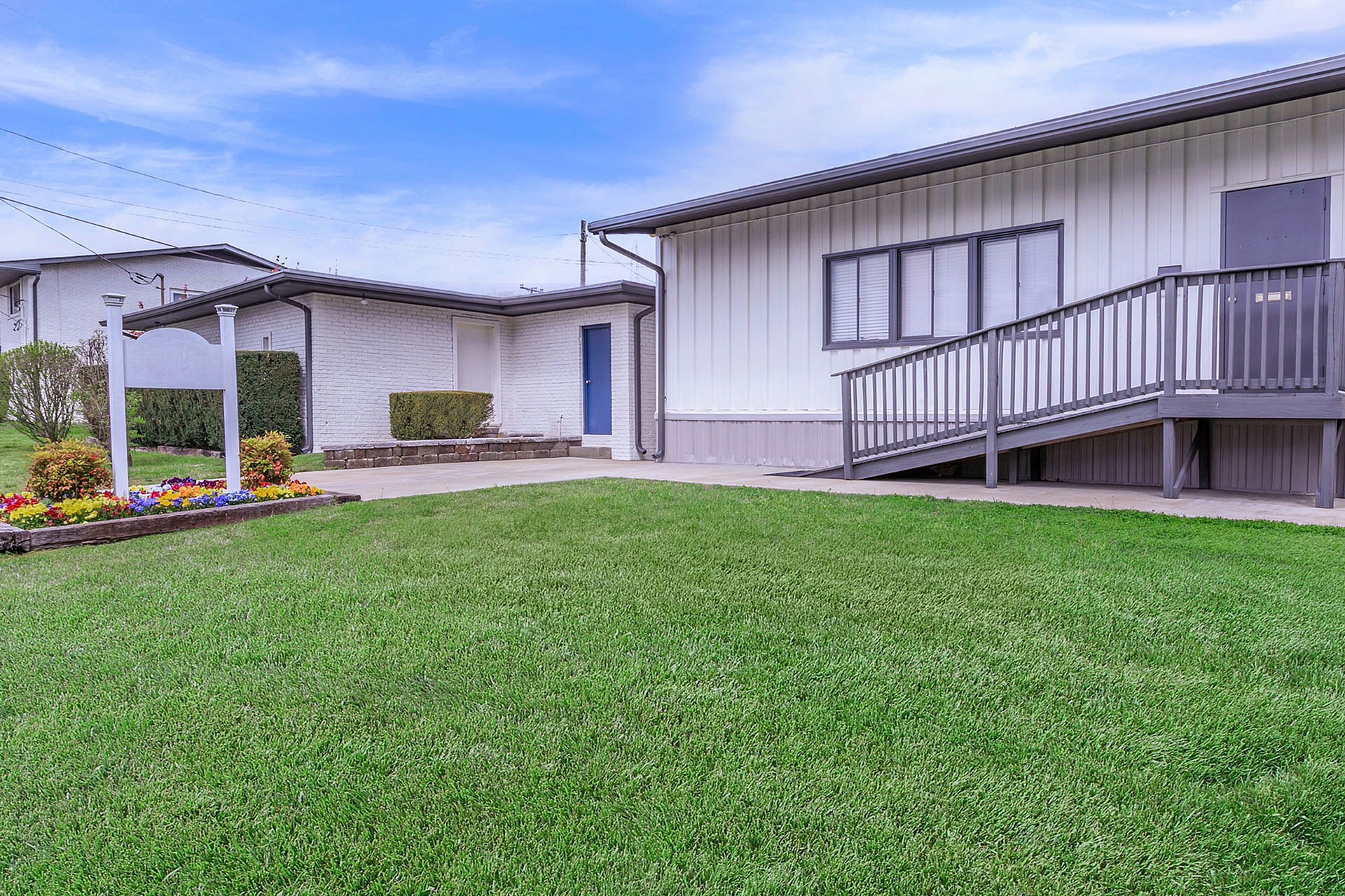 Charming white building with modern ramp entrance, surrounded by lush green lawn and colorful flower bed.